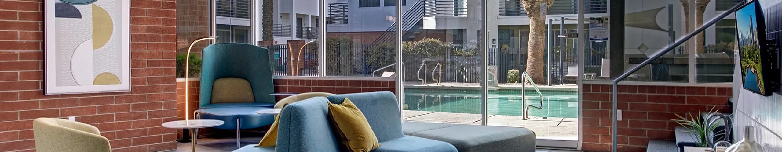 Chic apartment lounge with modern seating, large glass windows offering pool view, and vibrant decor.
