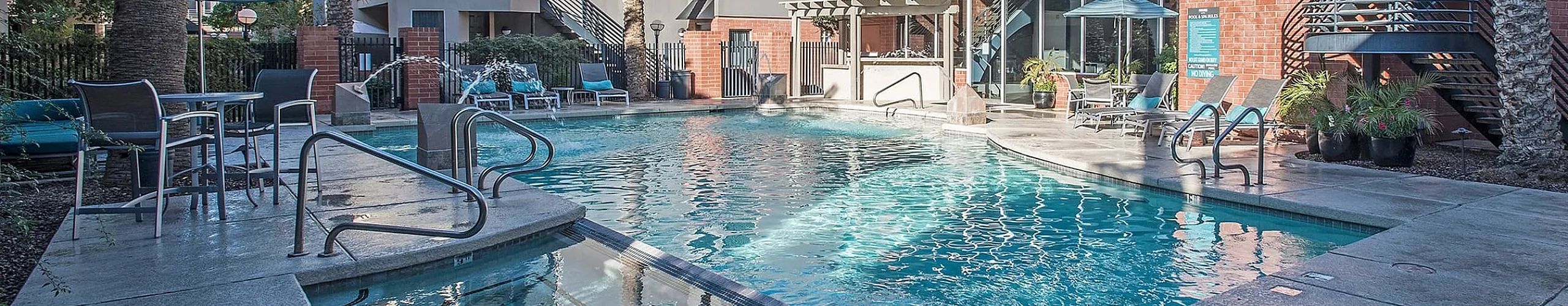 Luxurious apartment complex featuring a sparkling swimming pool surrounded by palm trees and stylish outdoor seating, ideal for relaxation in a sunny locale.