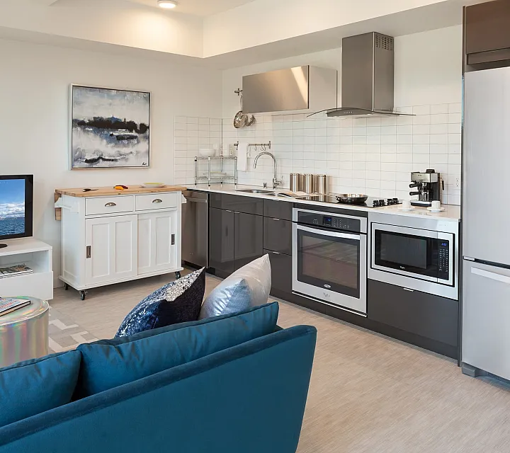 Chic modern kitchen and cozy living space with sleek appliances, vibrant blue sofa, and artistic decor.