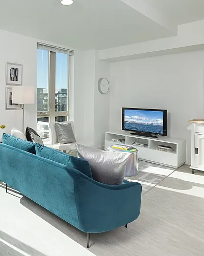 Bright, modern living room with vibrant decor, featuring a plush teal sofa, glass-top dining table, and expansive views through large windows.