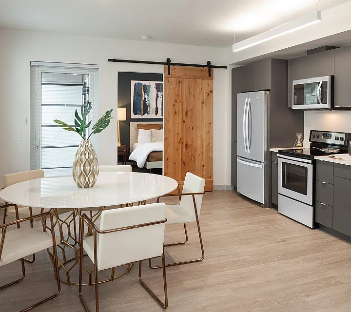 Modern kitchen and dining area showcasing sleek cabinetry, stainless steel appliances, and elegant decor. Features sliding barn door leading to a cozy bedroom.