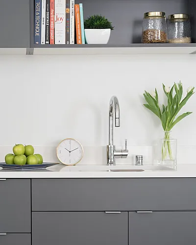 Modern kitchen with sleek grey cabinets, stainless steel appliances, and chic decor including a bowl of green apples and fresh flowers.