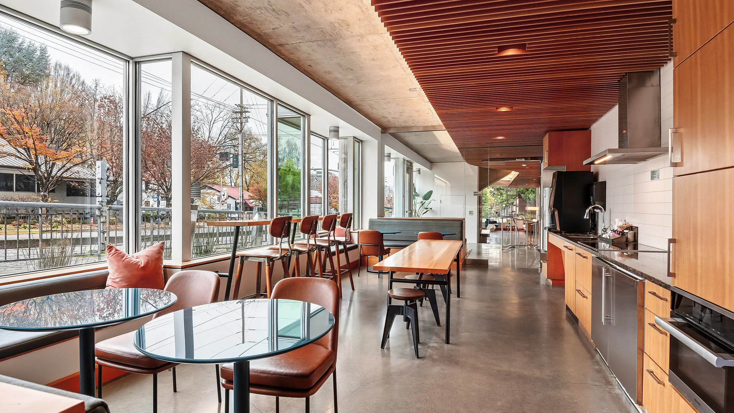 Modern open-concept apartment interior with sleek kitchen, stylish dining area, and expansive windows showcasing a vibrant street view.