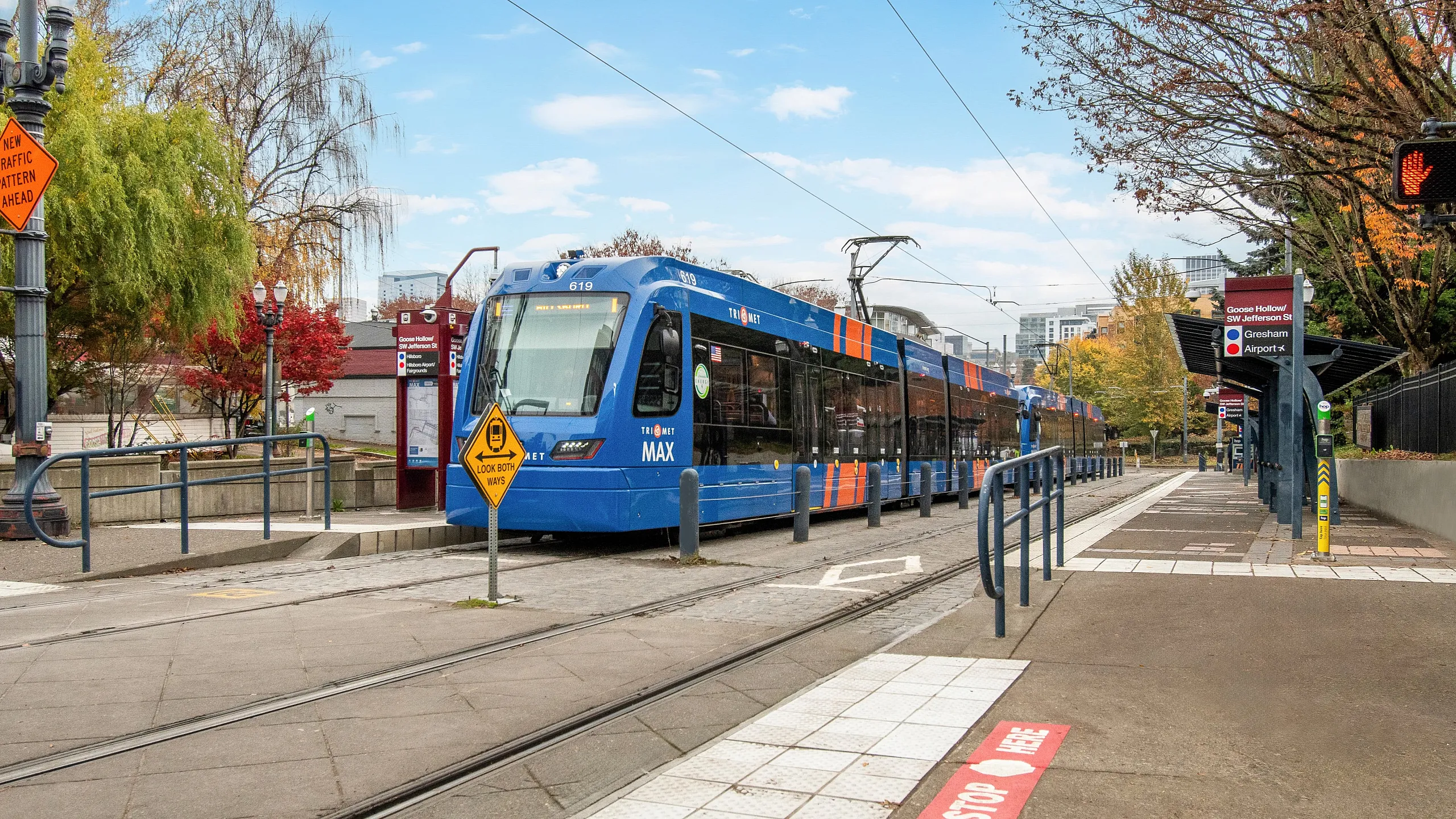 Vibrant cityscape with a sleek blue tram at a modern transit stop, surrounded by colorful autumn trees.