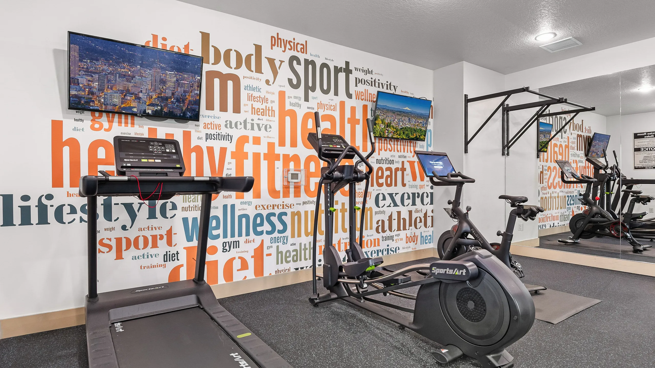 Modern apartment gym featuring state-of-the-art exercise equipment including a treadmill, elliptical, and bike, with vibrant word art promoting fitness and wellness.