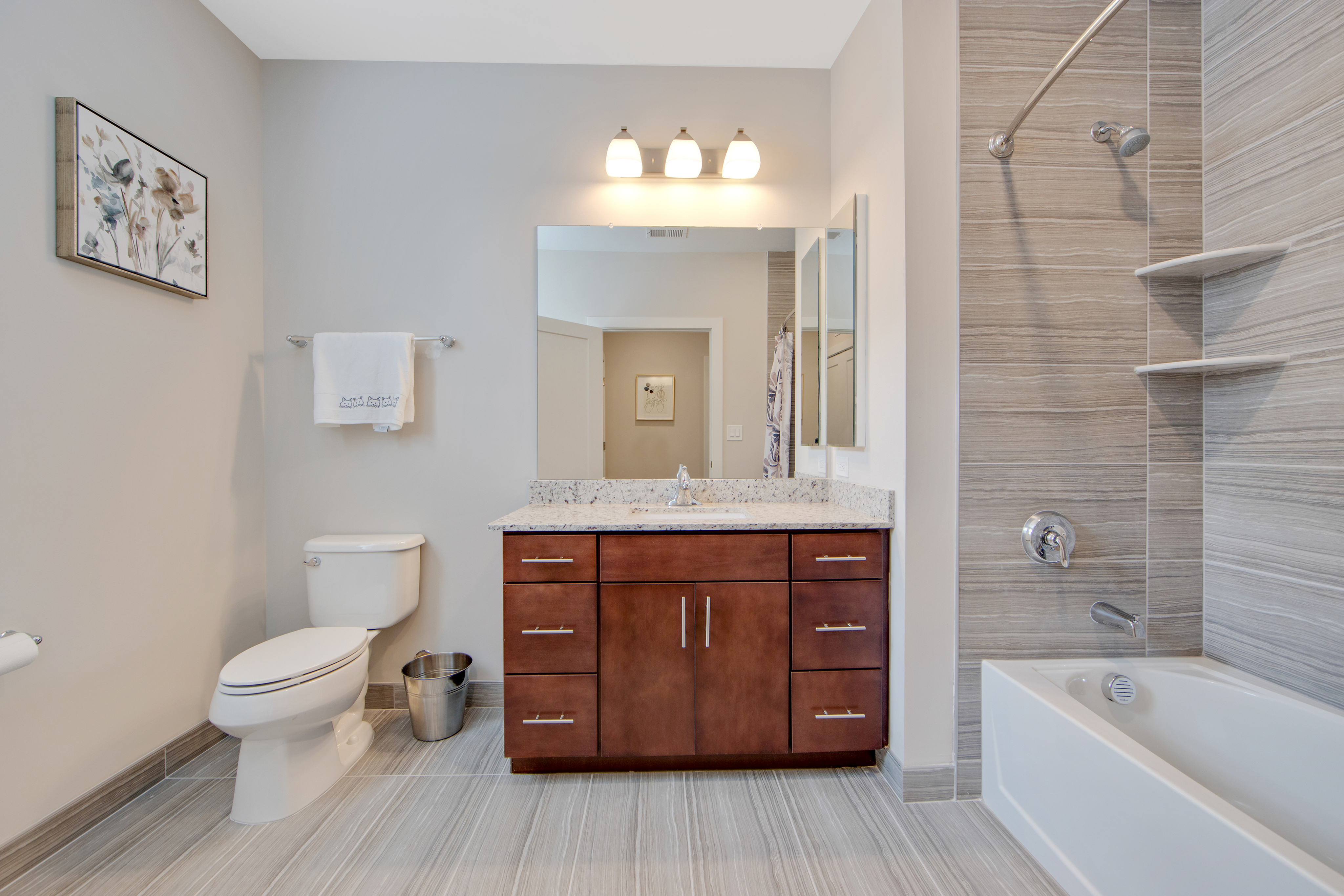 Modern bathroom with elegant wooden vanity, granite countertop, and luxurious bathtub surrounded by stylish tiling.