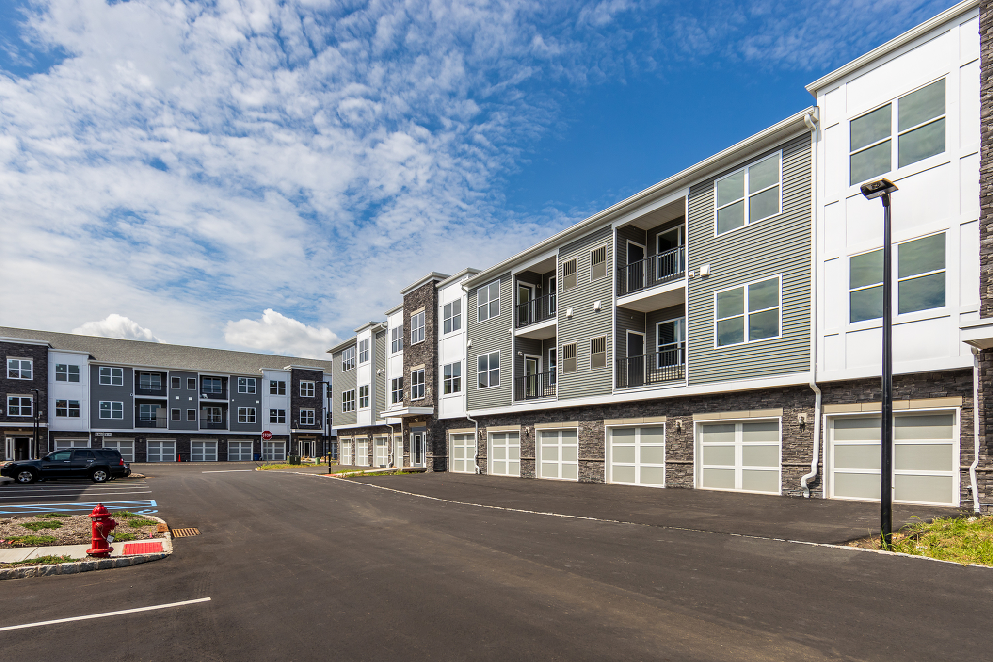 Modern three-story apartment complex with spacious balconies, ample parking, and elegant stone accents under a vibrant blue sky.