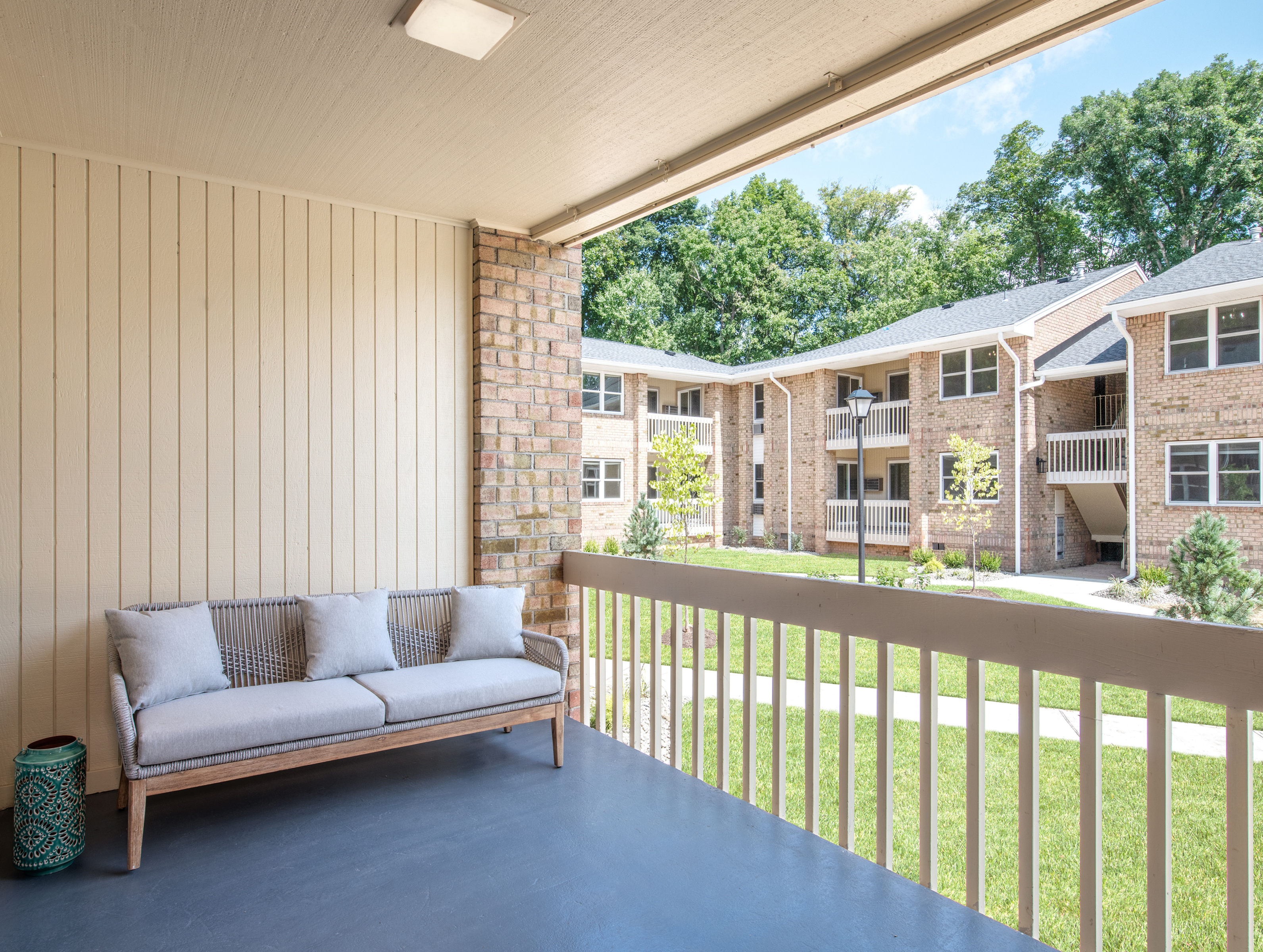 Charming apartment balcony with cozy seating overlooking lush green courtyard and classic brick architecture.