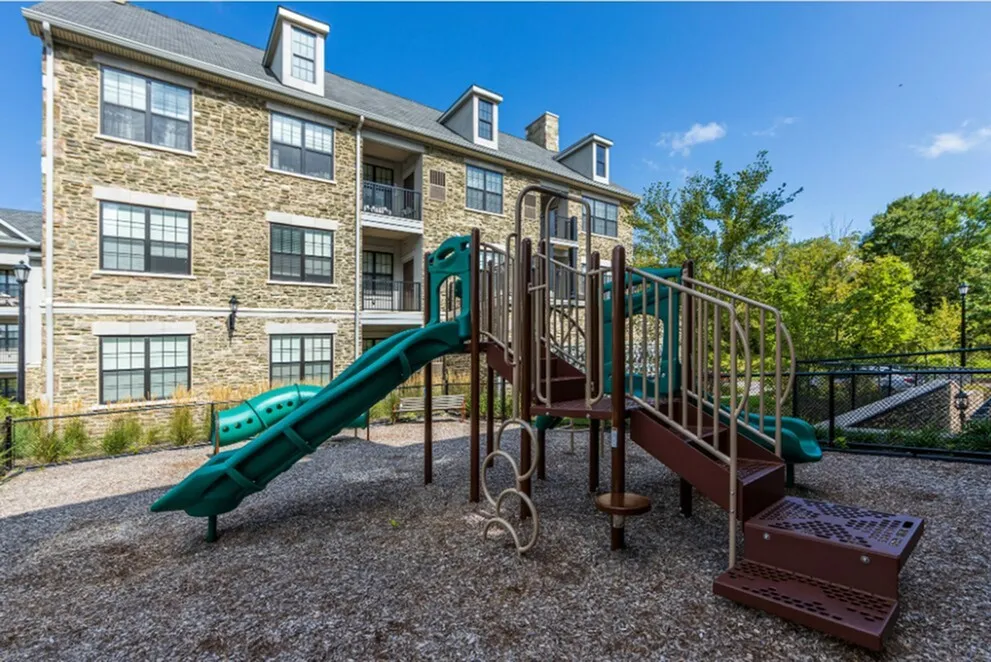 Charming apartment building with a delightful playground area, perfect for families, surrounded by lush greenery and a bright blue sky.
