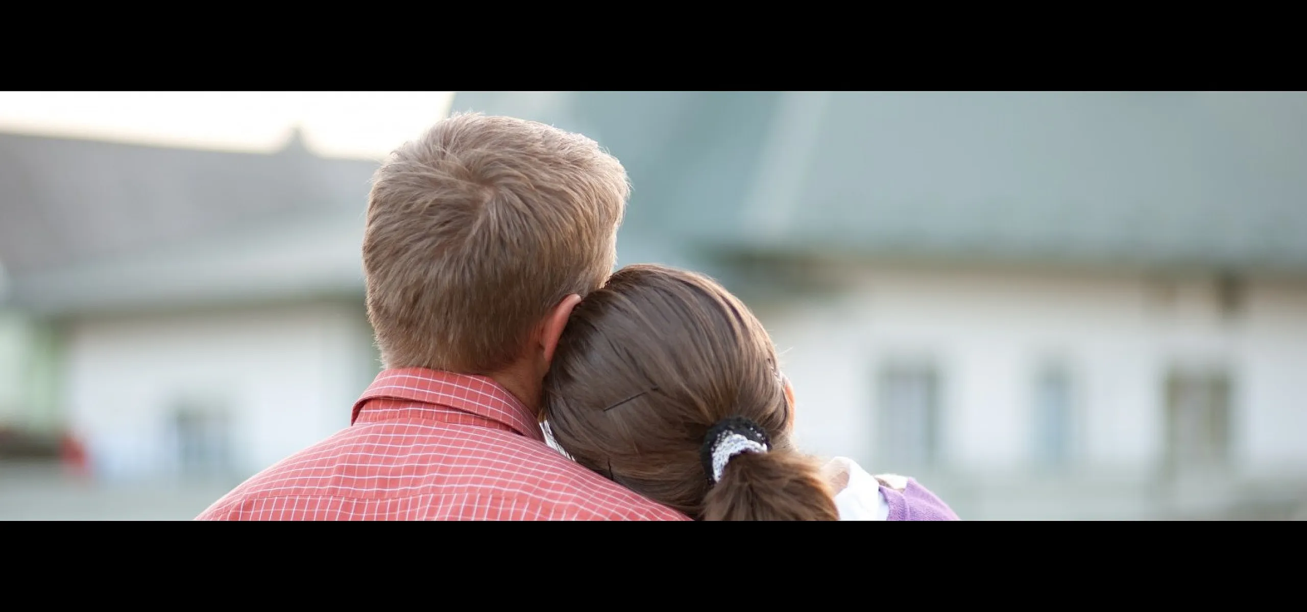 Couple embracing with a view of cozy suburban homes, conveying warmth and a welcoming neighborhood atmosphere.