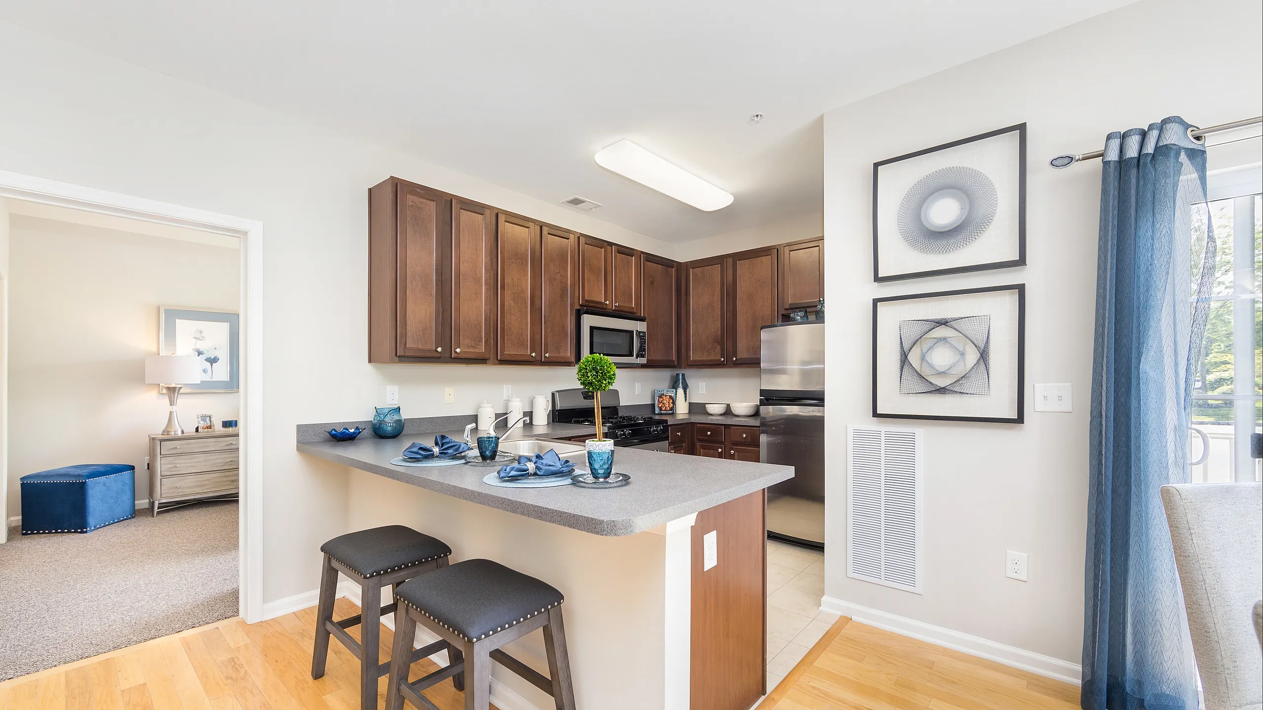 Modern kitchen with wooden cabinets, sleek countertops, and bar seating, opening into a beautifully decorated living area with elegant decor.