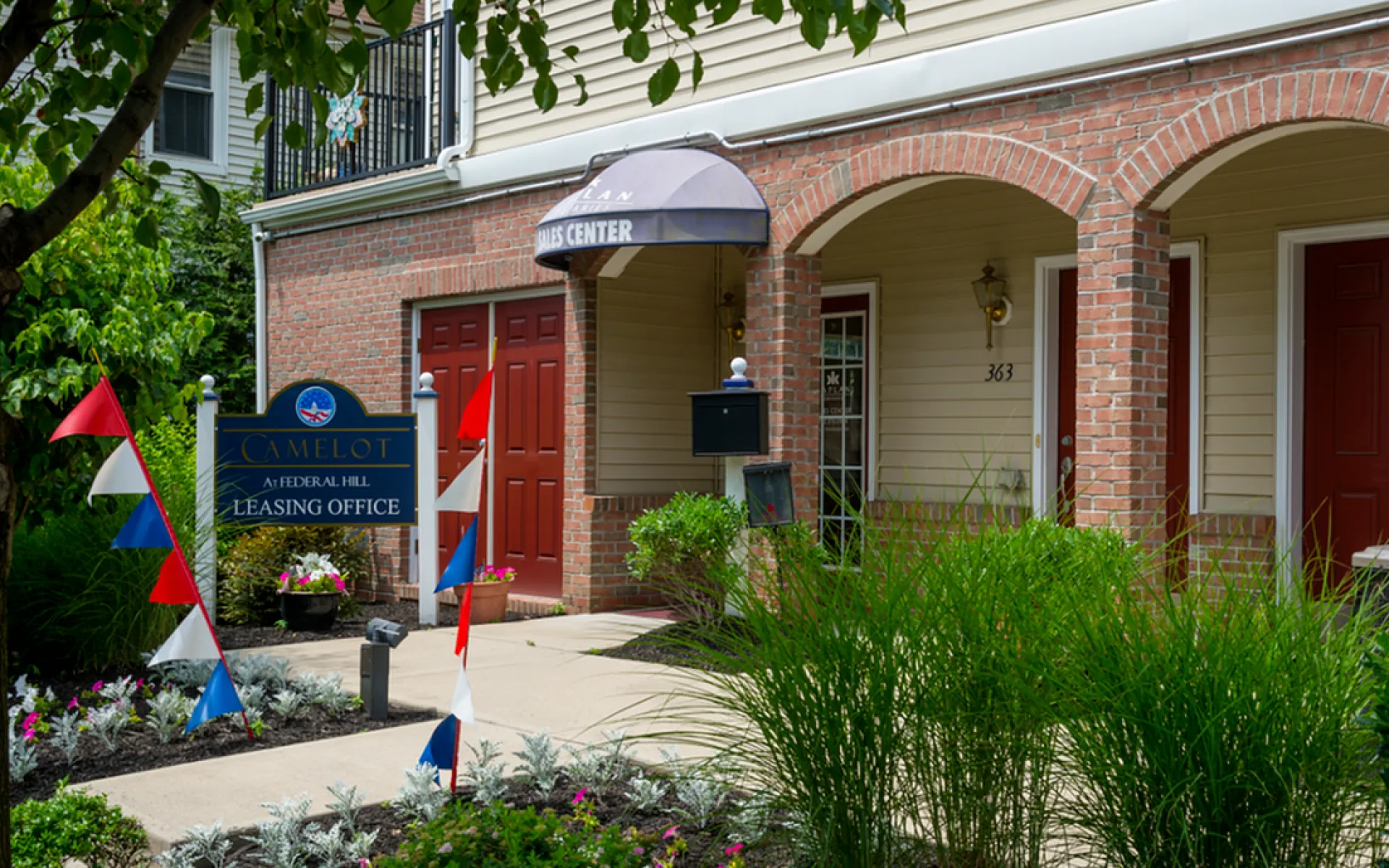 Inviting leasing office entrance at Camelot with vibrant signage and lush landscaping.