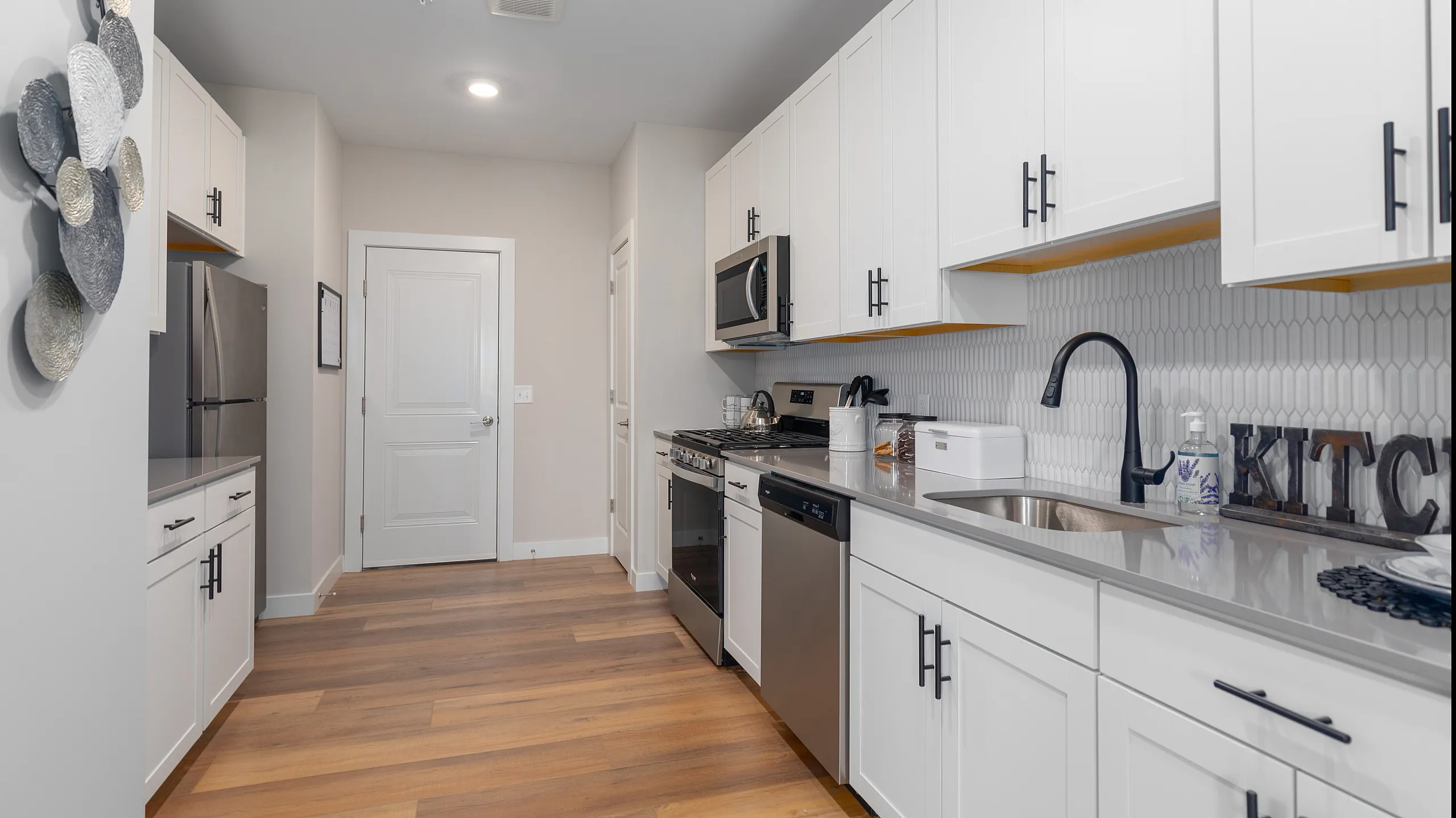 Modern kitchen with sleek white cabinets, stainless steel appliances, and elegant wooden flooring, exuding a bright and contemporary atmosphere.