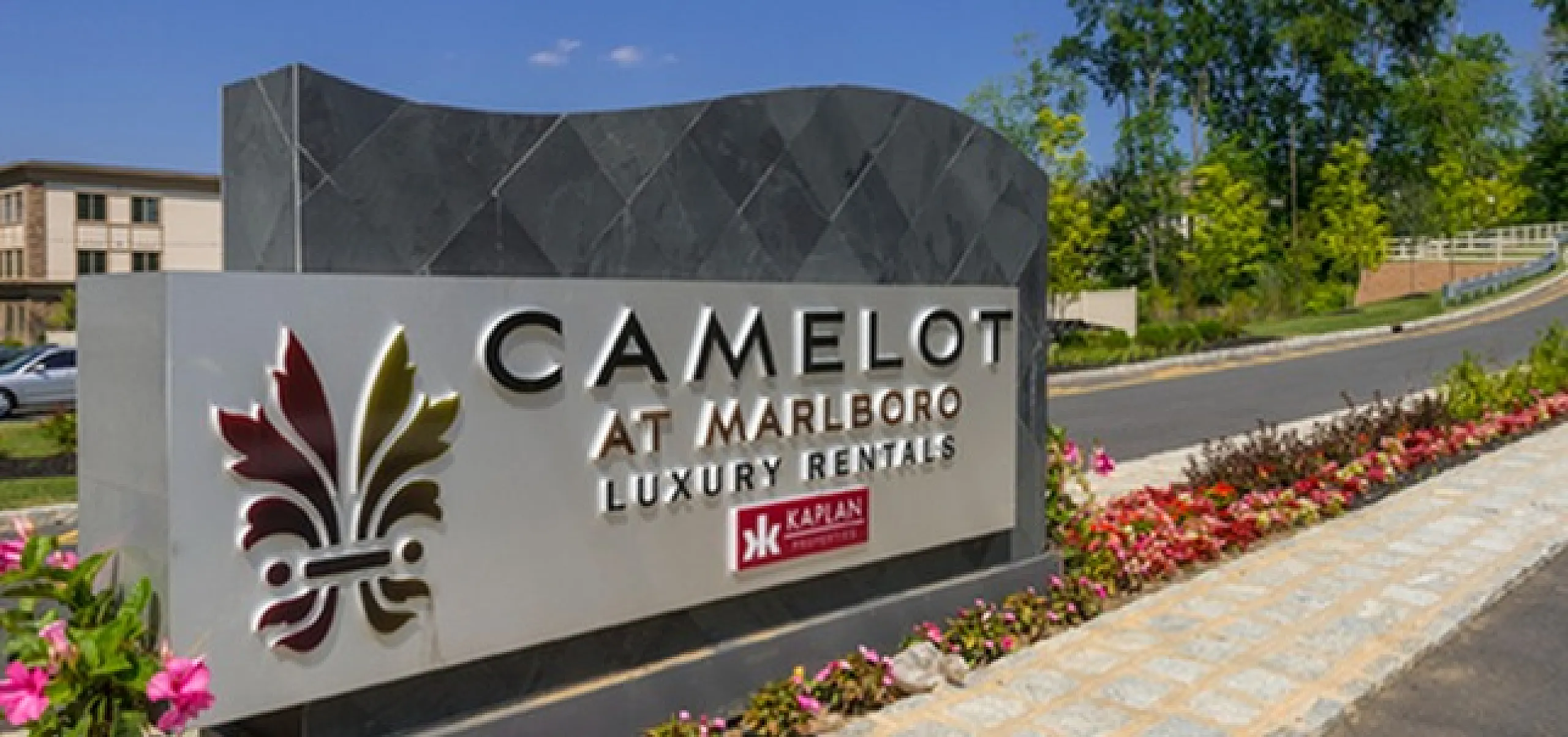 Inviting entrance sign for Camelot at Marlboro Luxury Rentals surrounded by vibrant flowers and clear blue skies, showcasing upscale living.
