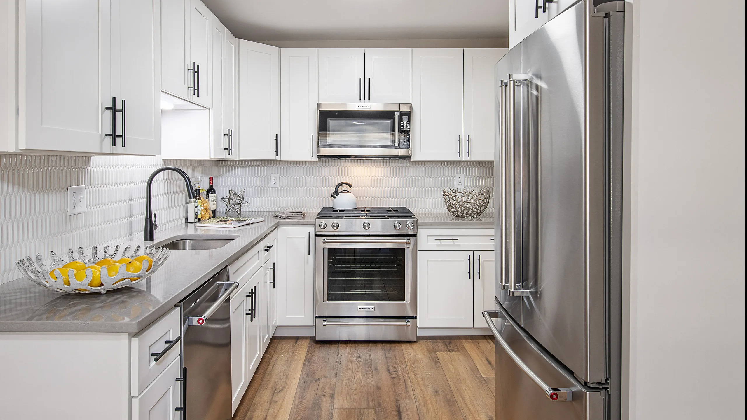 Modern kitchen showcasing sleek white cabinetry, stainless steel appliances, and elegant wood flooring.