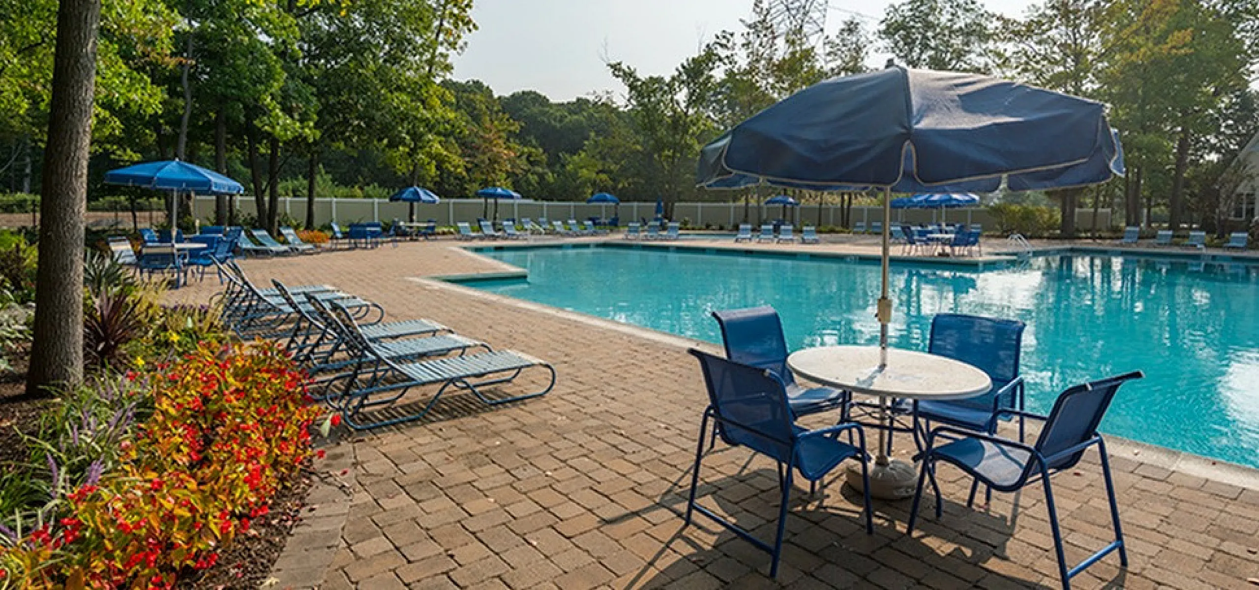 Inviting outdoor pool area with lush greenery, elegant loungers, and stylish blue umbrellas, perfect for relaxation and enjoyment.