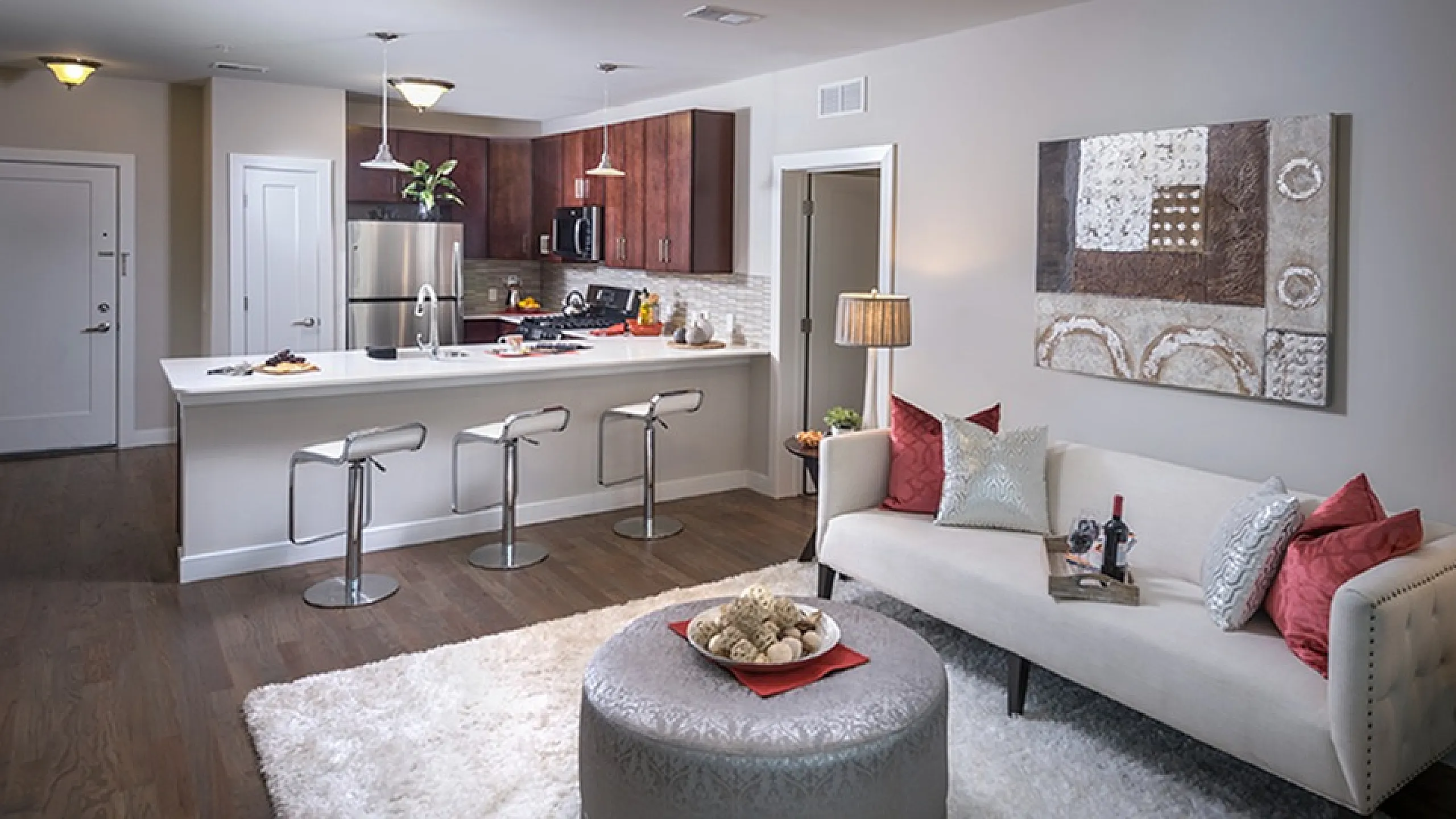 Modern open-concept living room and kitchen with elegant decor, featuring a cozy sofa, stylish artwork, and sleek bar stools around a spacious island.