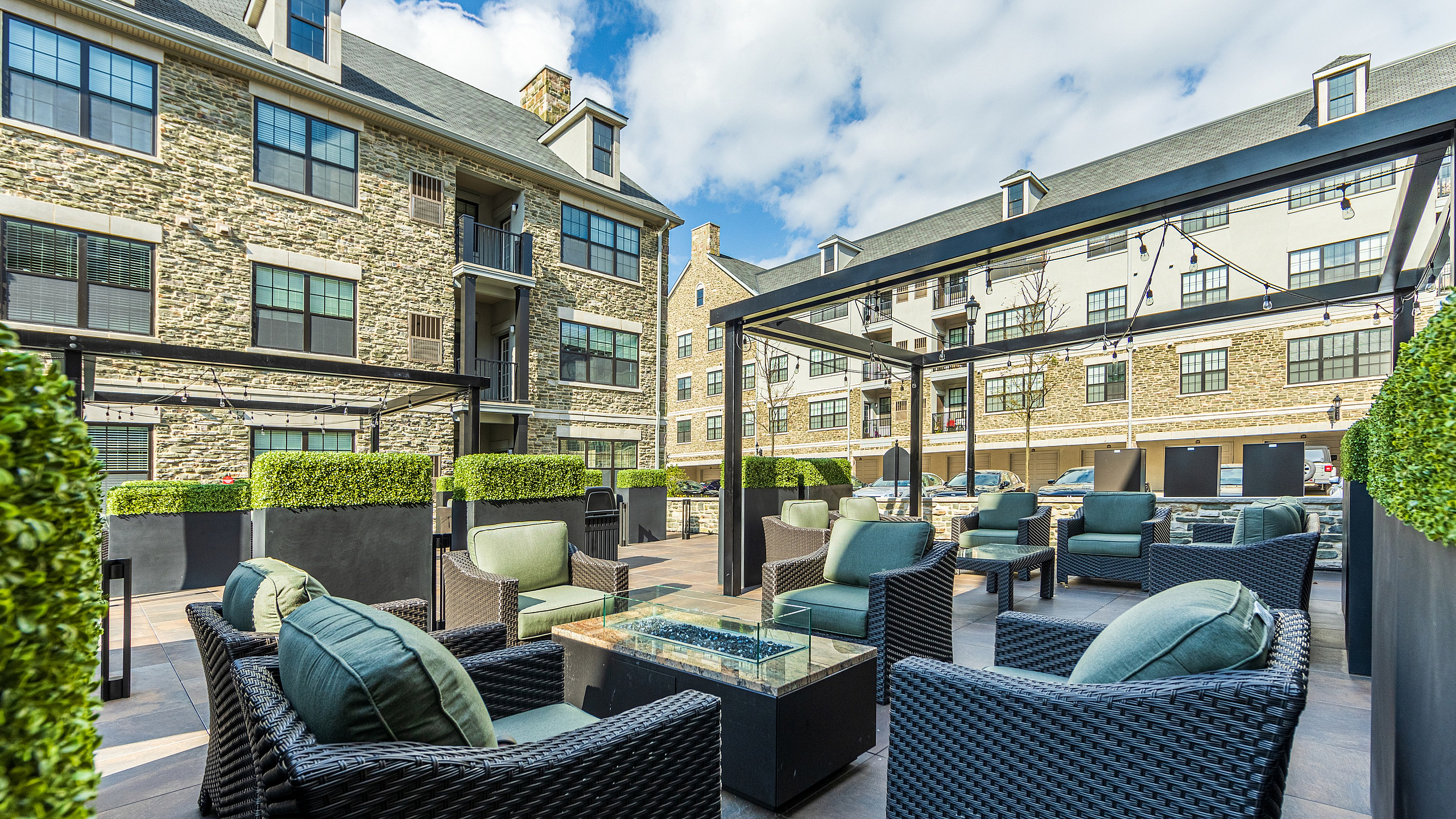 Chic outdoor courtyard with stylish wicker seating and lush greenery at a modern apartment complex.