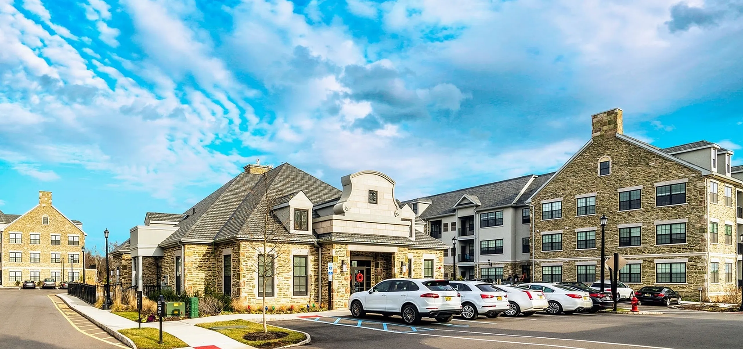 Charming stone-clad apartment complex with ample parking and lush landscaping under a bright blue sky.