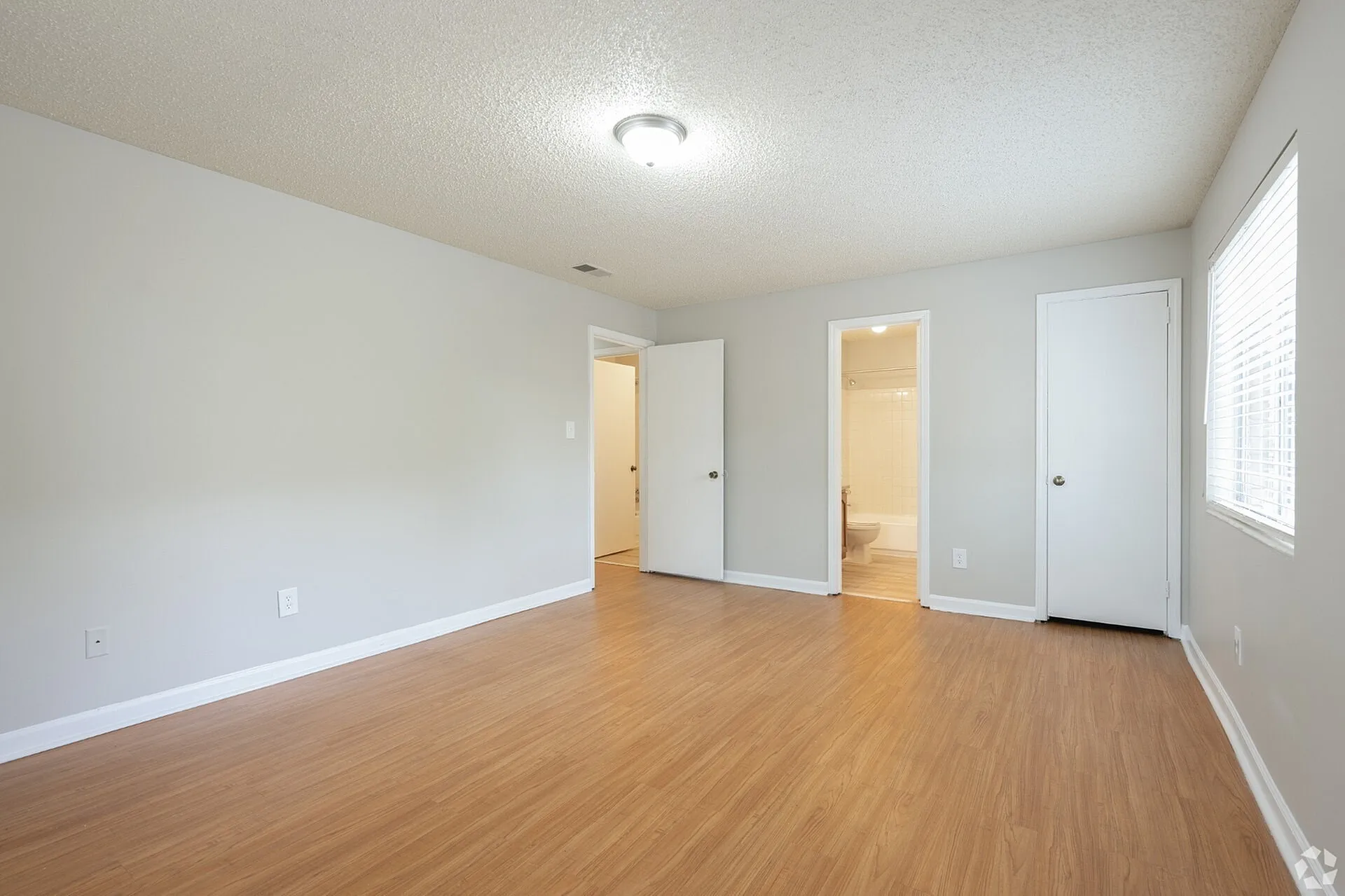 Bright and spacious bedroom with elegant wooden flooring, featuring ample natural light and an attached bathroom.