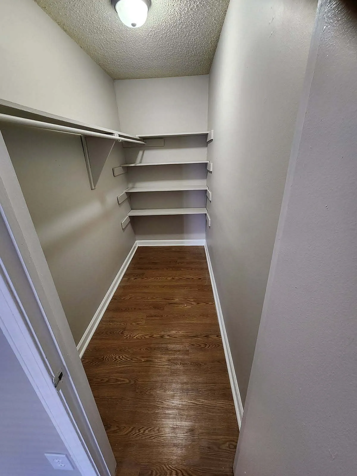 Spacious walk-in closet with elegant wooden flooring and ample shelving, ideal for organized living.