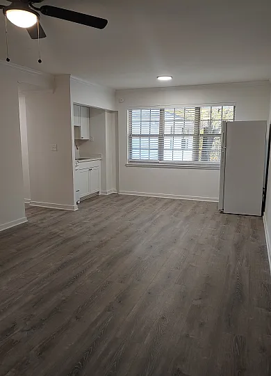 Bright and inviting open-plan living space featuring elegant wood flooring, modern ceiling fan, and sunlit window with sleek white kitchen cabinetry.