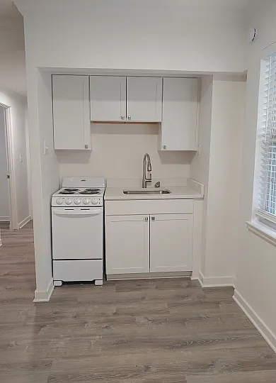 Charming compact kitchen with sleek white cabinets, modern stove, and elegant sink, perfectly blending functionality and style.