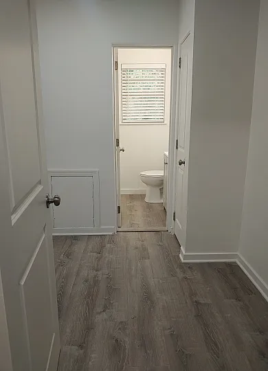 Inviting hallway leading to a bright bathroom with modern wood flooring and pristine white walls, perfect for a cozy home ambiance.
