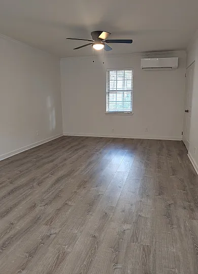 Spacious and bright living area with elegant wood flooring, a modern ceiling fan, and ample natural light.