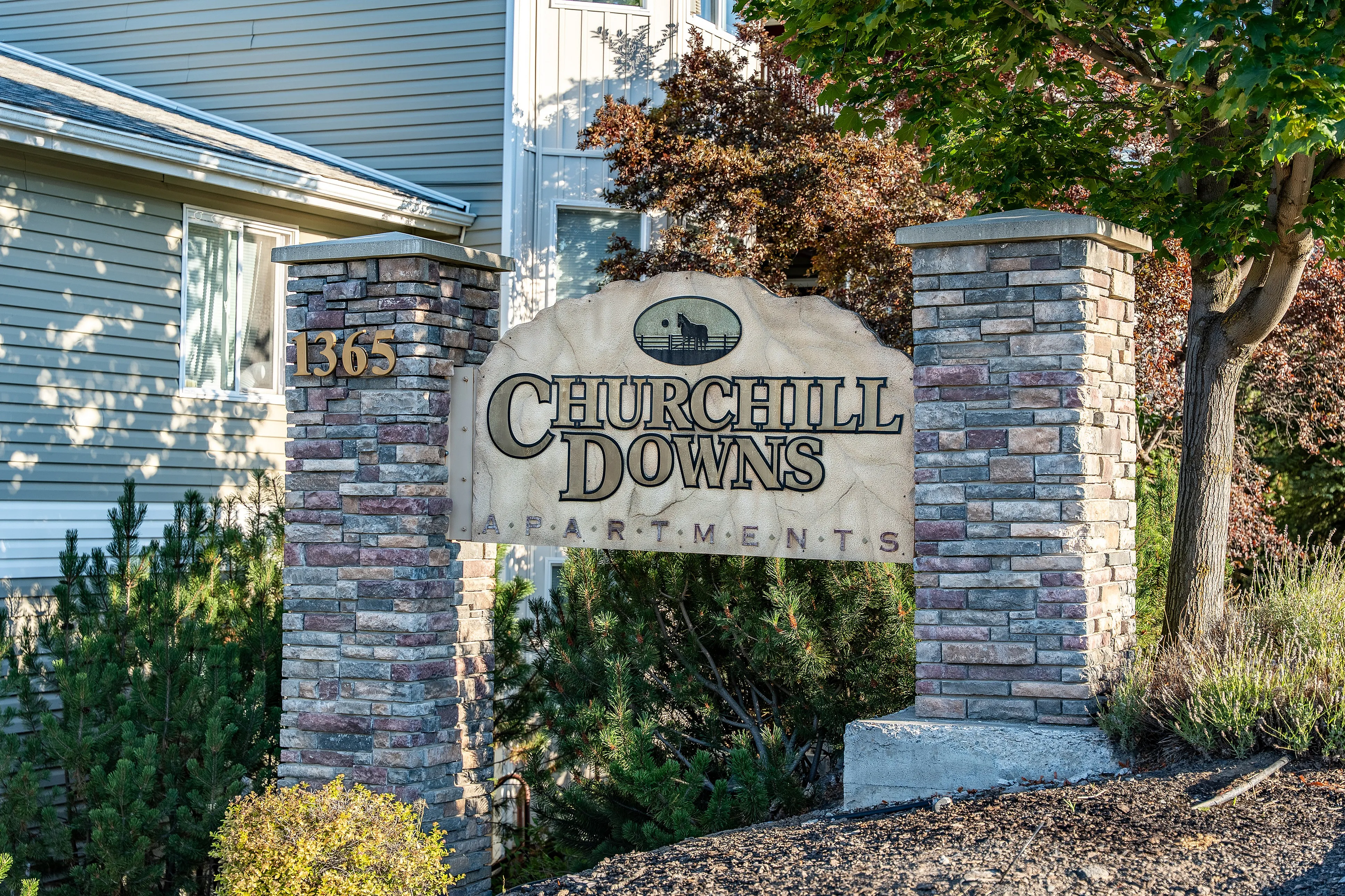Elegant entrance sign for Churchill Downs Apartments featuring a stone column and lush greenery.