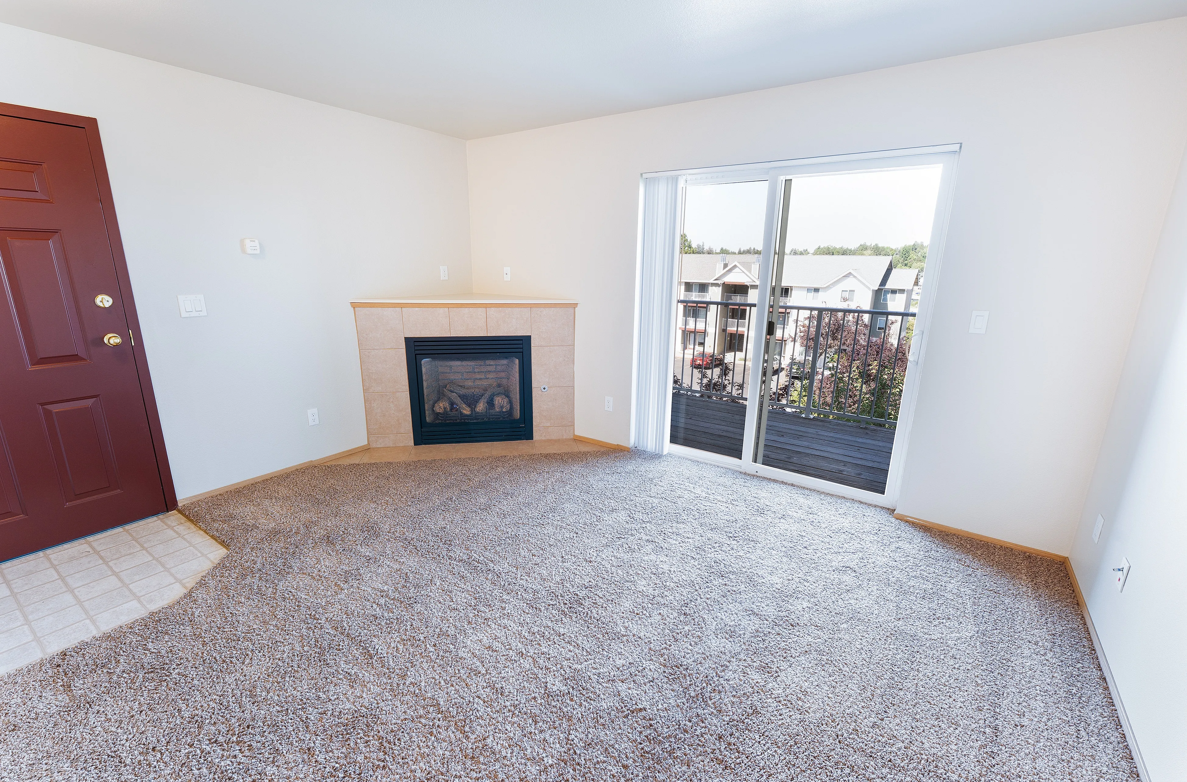 Inviting apartment living room with cozy carpet, elegant fireplace, and bright sliding doors opening to a scenic balcony view.