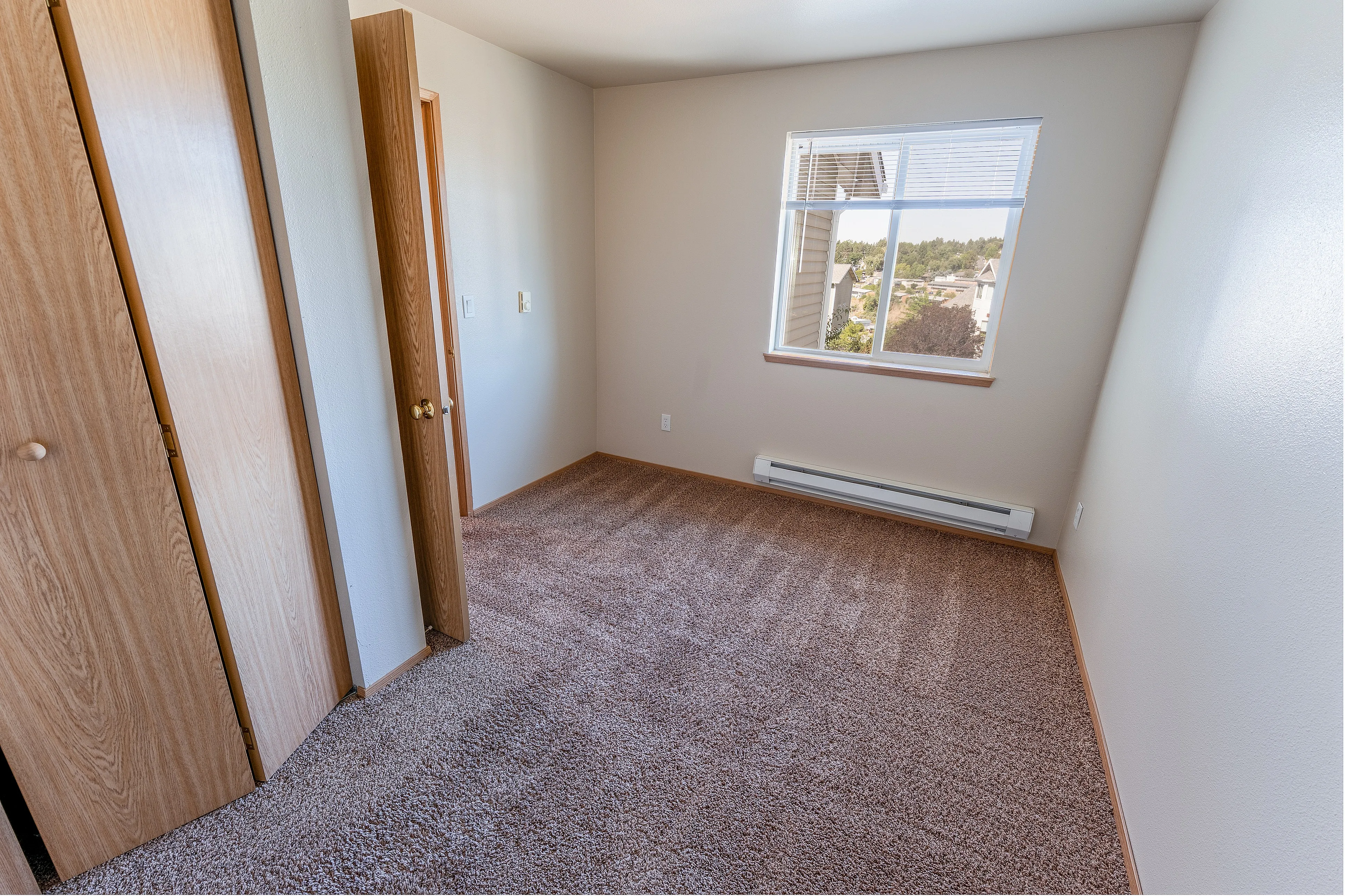 Cozy sunlit bedroom with plush carpeting, wooden closet doors, and a scenic window view for natural light and warmth.