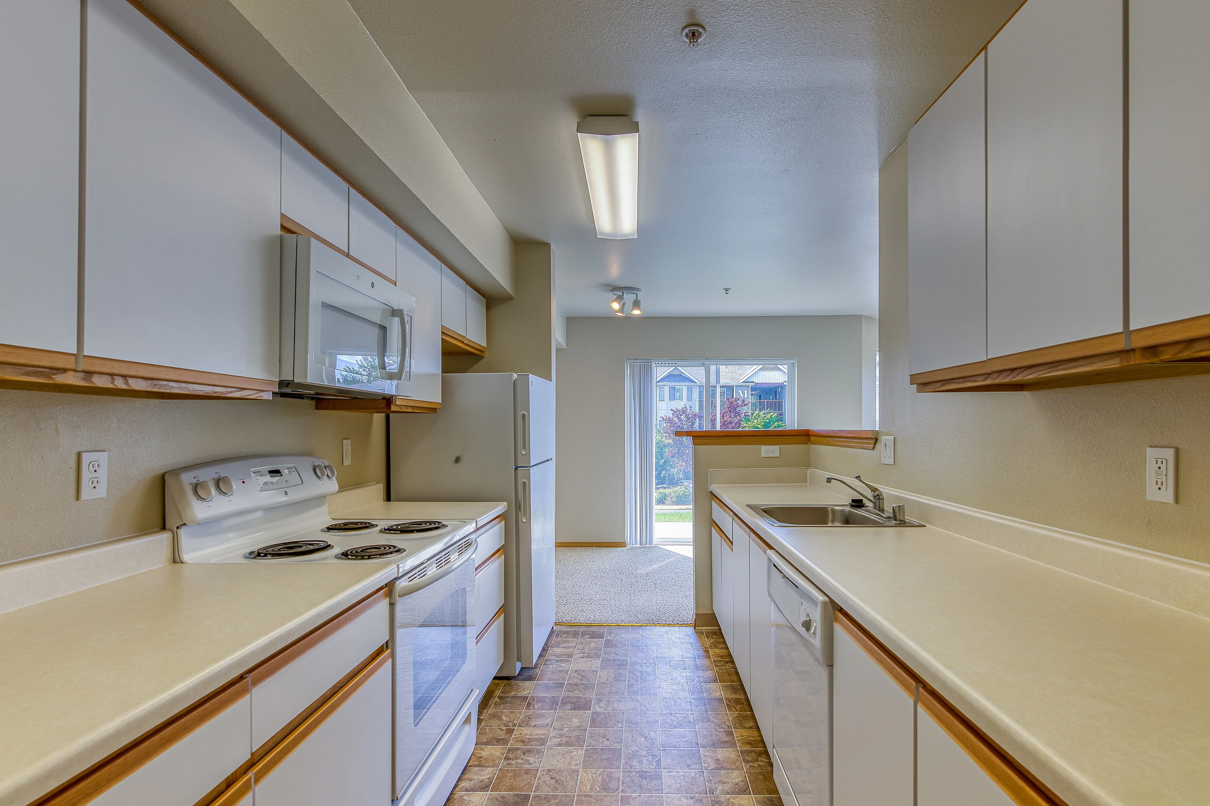 Bright and modern kitchen with white cabinetry, sleek countertops, and a window view of green landscape.