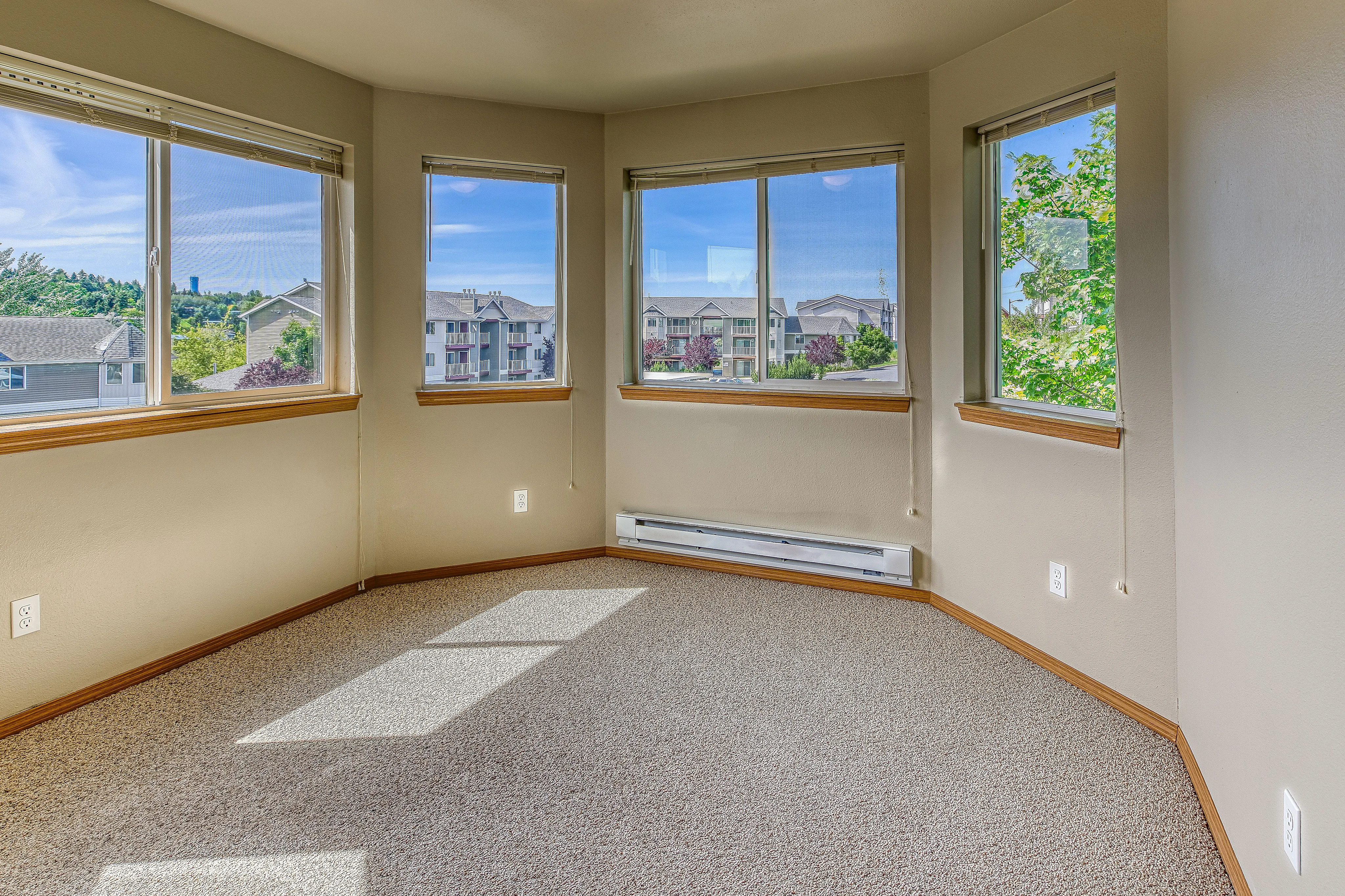 Bright and inviting corner room with large windows offering beautiful views of lush greenery and neighboring buildings.
