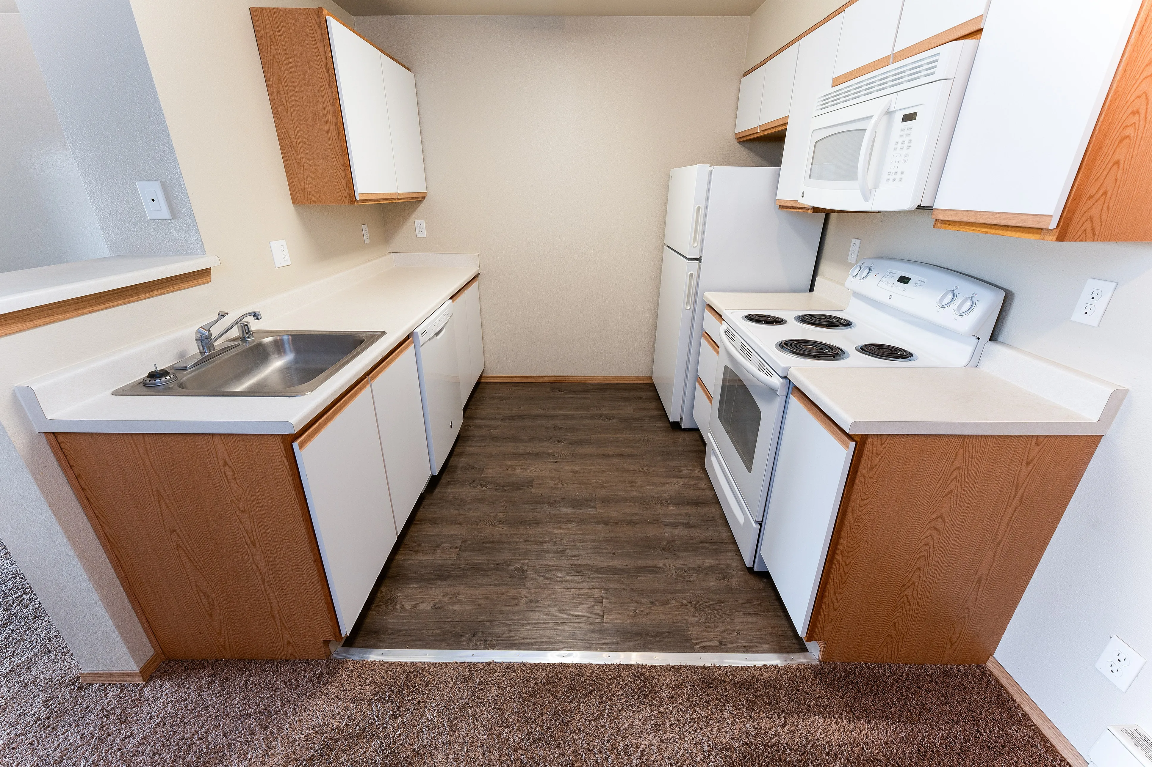 Modern kitchen with sleek wooden cabinets, stainless steel sink, and white appliances, featuring stylish wood flooring.
