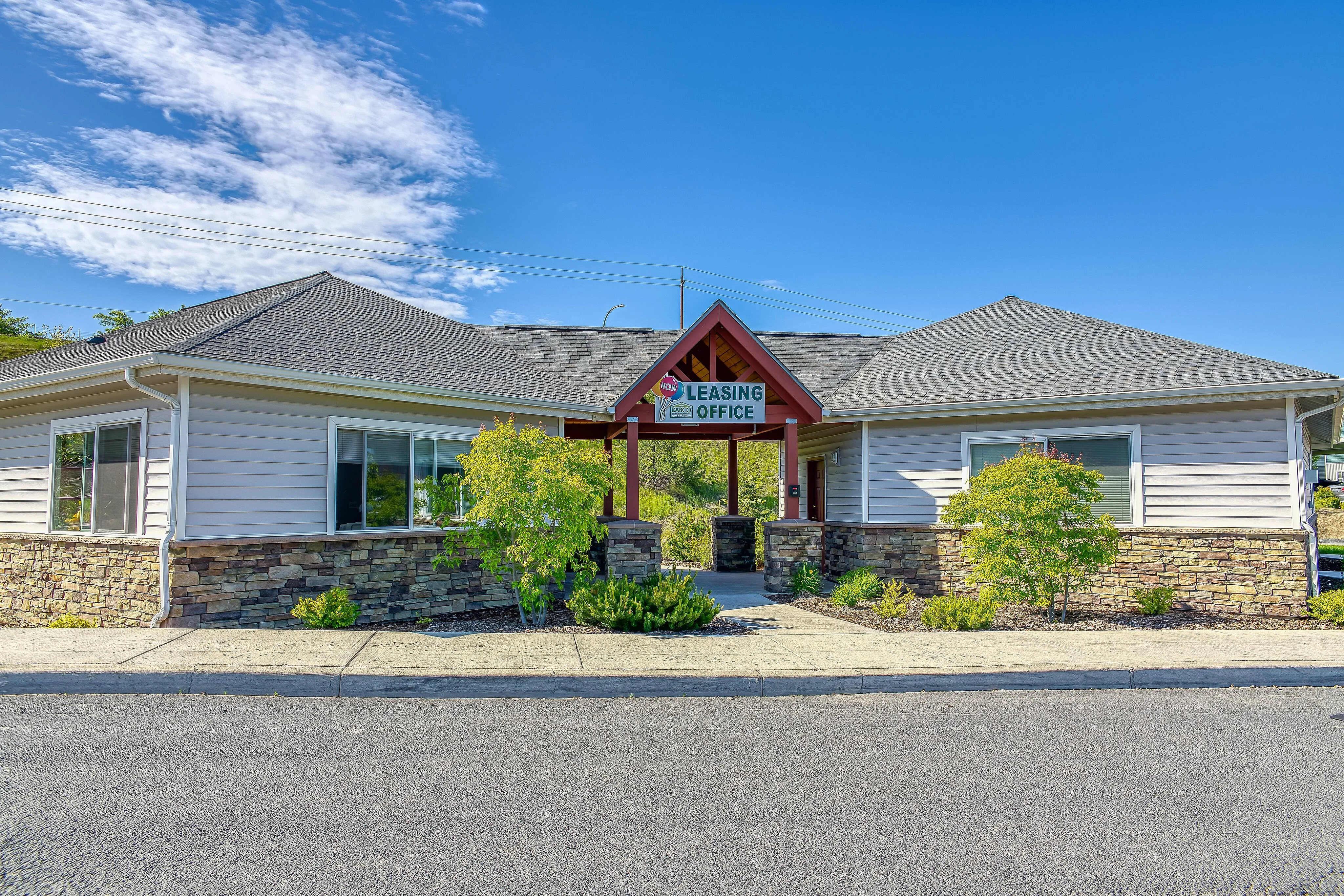 Inviting leasing office with a charming exterior, surrounded by lush greenery and clear blue skies.