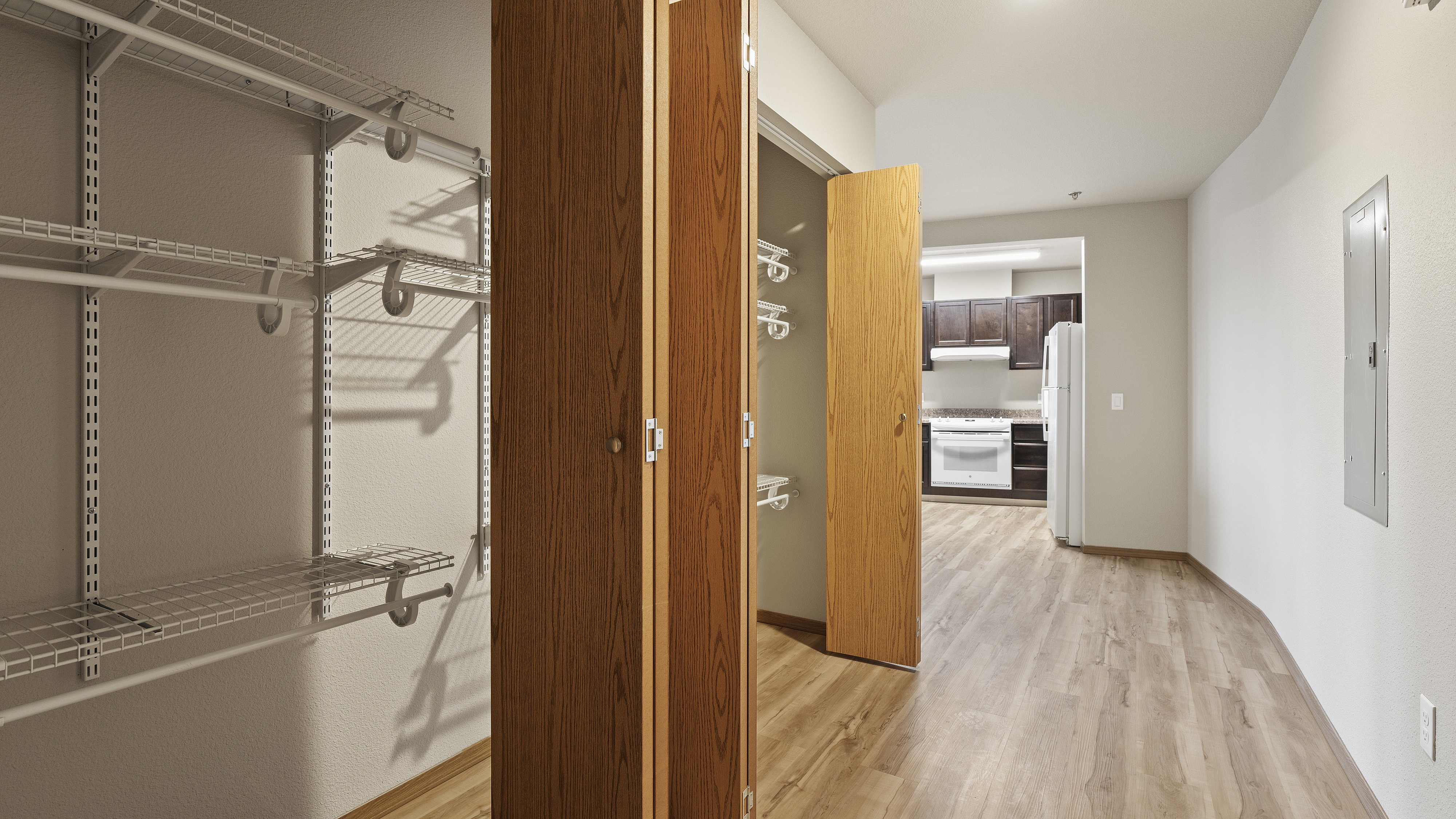 Inviting hallway with elegant wood flooring leading to an organized closet space and a modern kitchen with sleek dark cabinets.