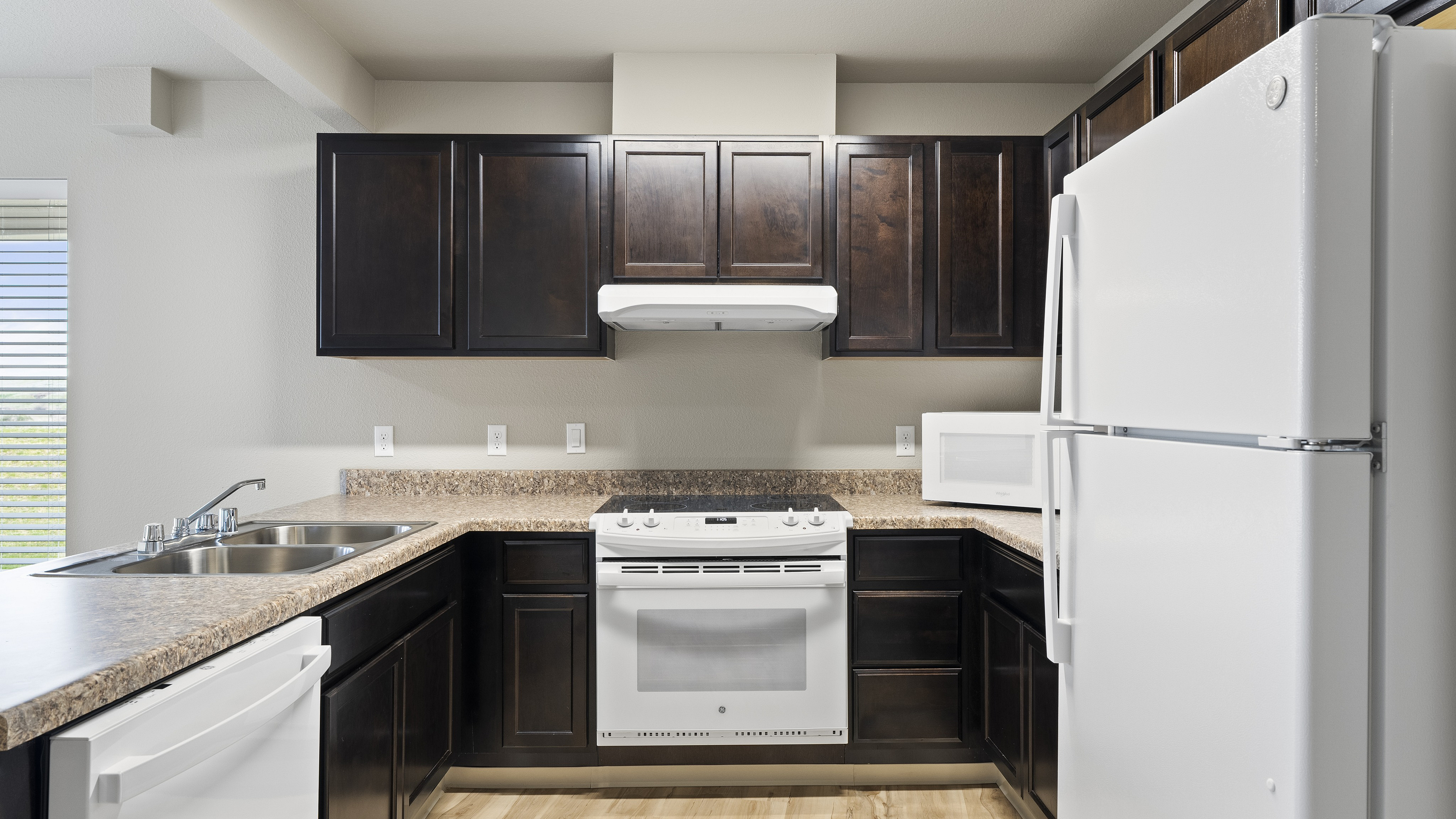 Modern kitchen with sleek dark wood cabinets, a spacious countertop, and new white appliances.
