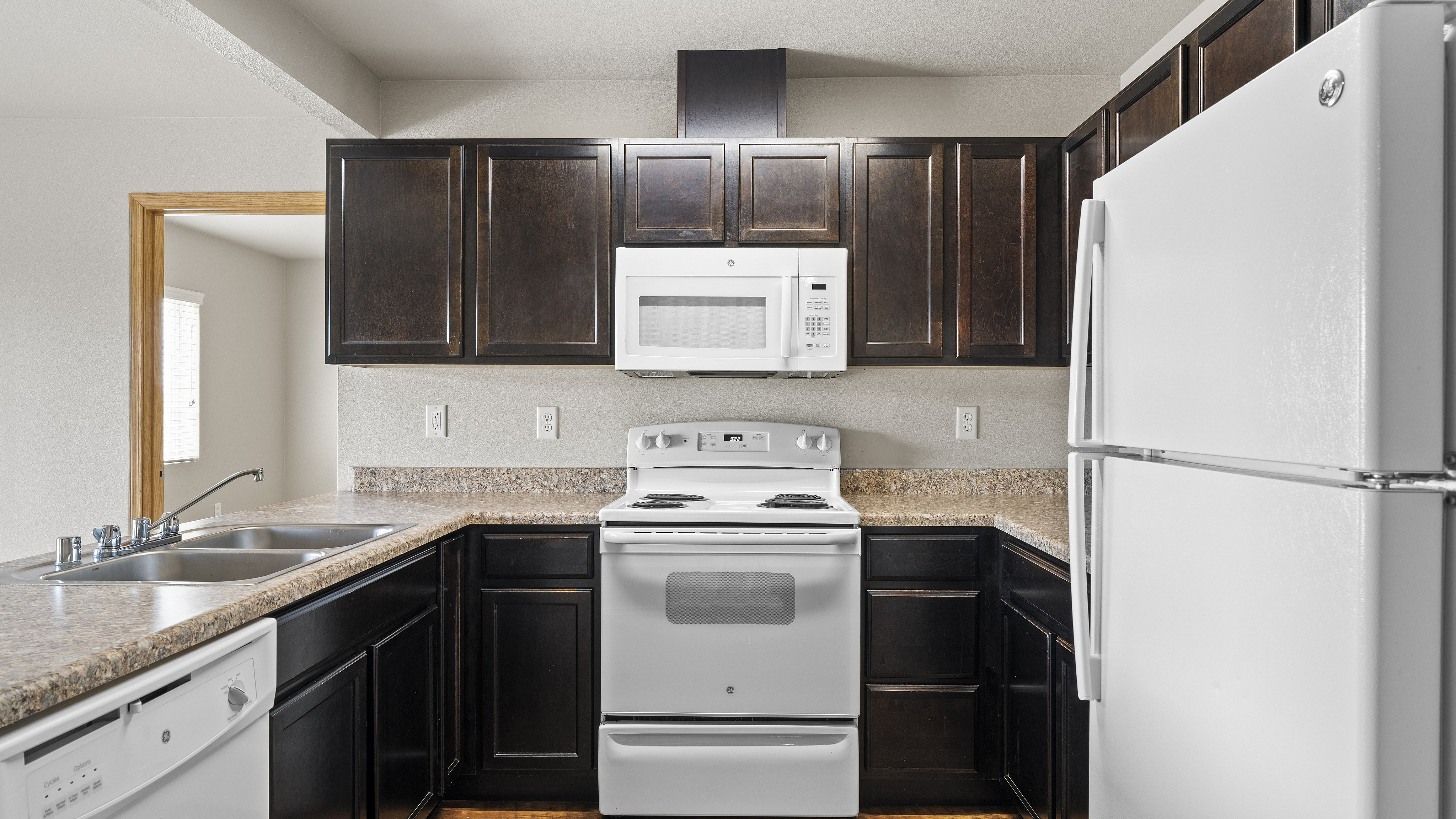Modern kitchen with sleek dark cabinets, a white fridge, microwave, and range, complemented by granite countertops.