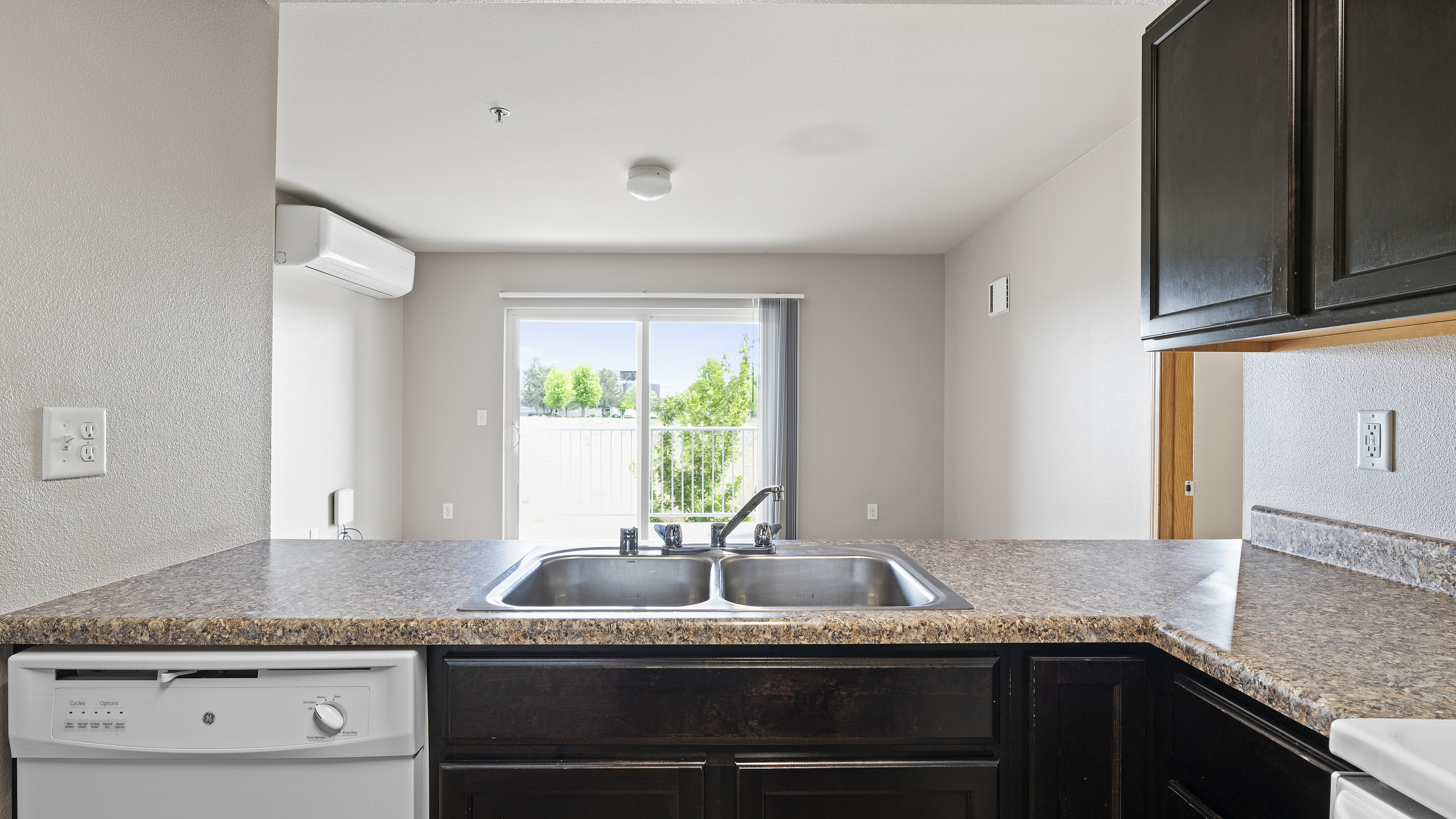 Bright kitchen with sleek countertops, dual sink, and a view of lush greenery through sliding glass doors.