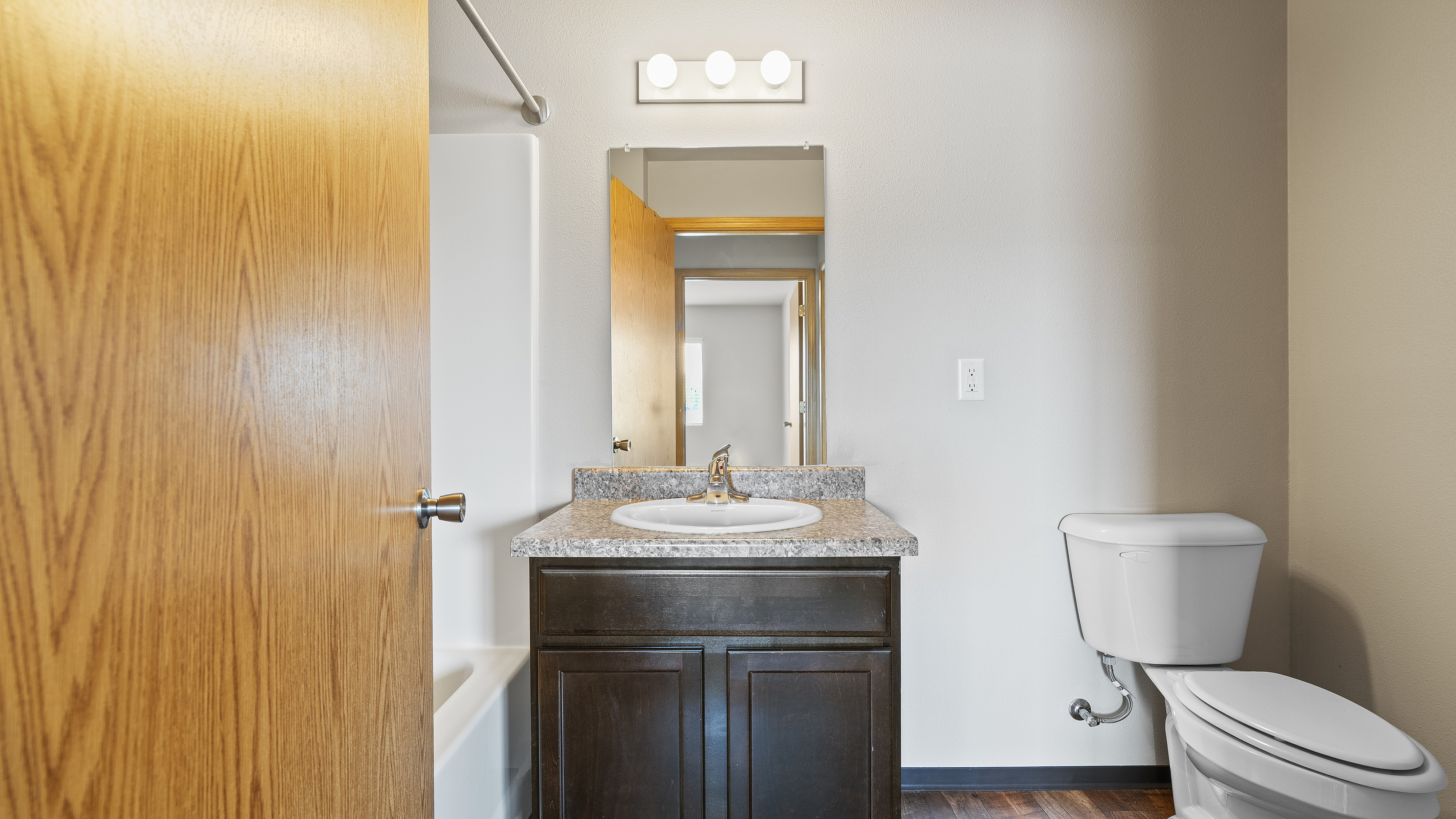 Modern bathroom with granite countertop sink, elegant vanity, and sleek toilet featuring a warm wood door.