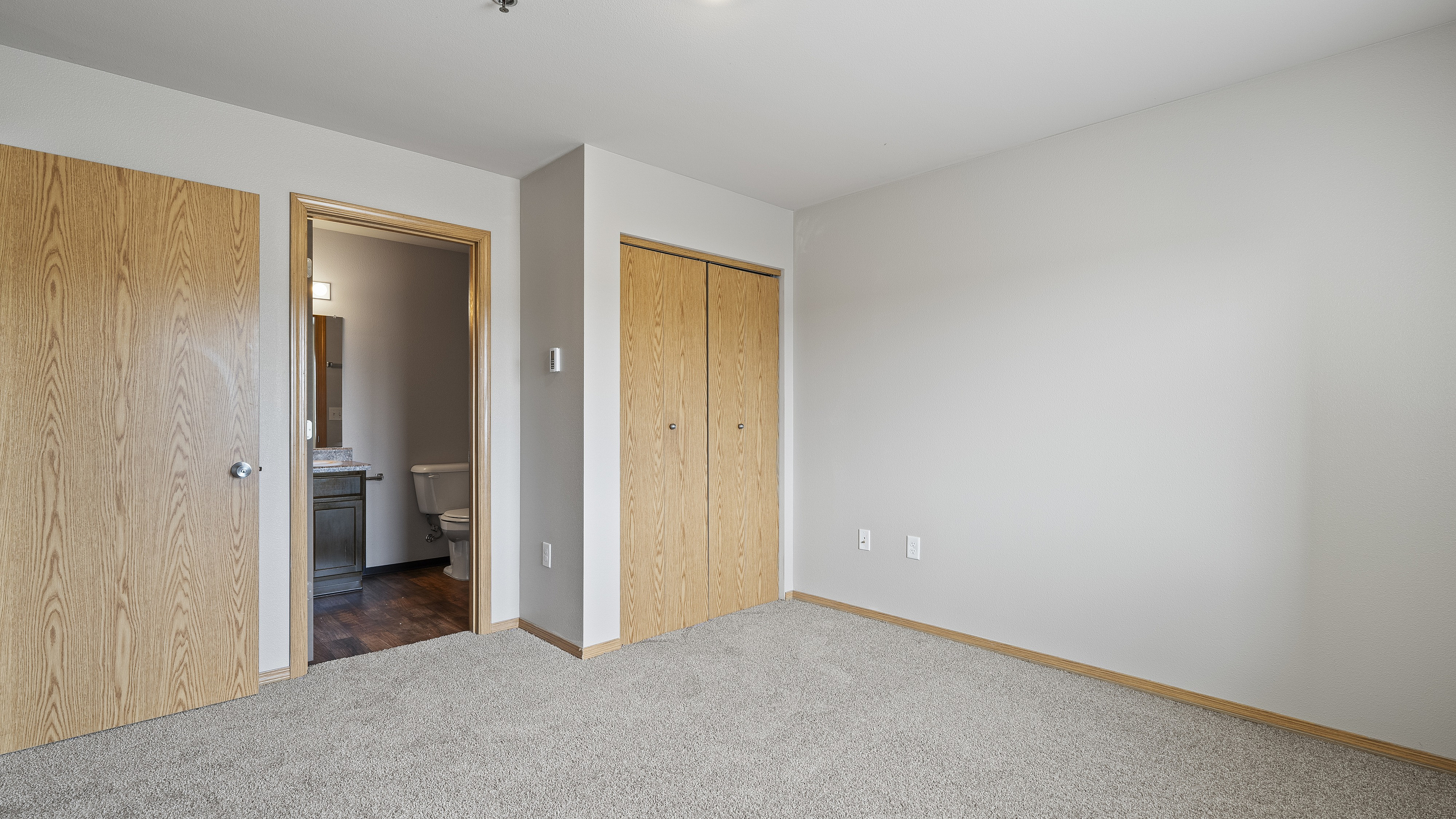Bright and inviting bedroom with neutral carpet, wooden doors, and attached bathroom, ideal for modern living.