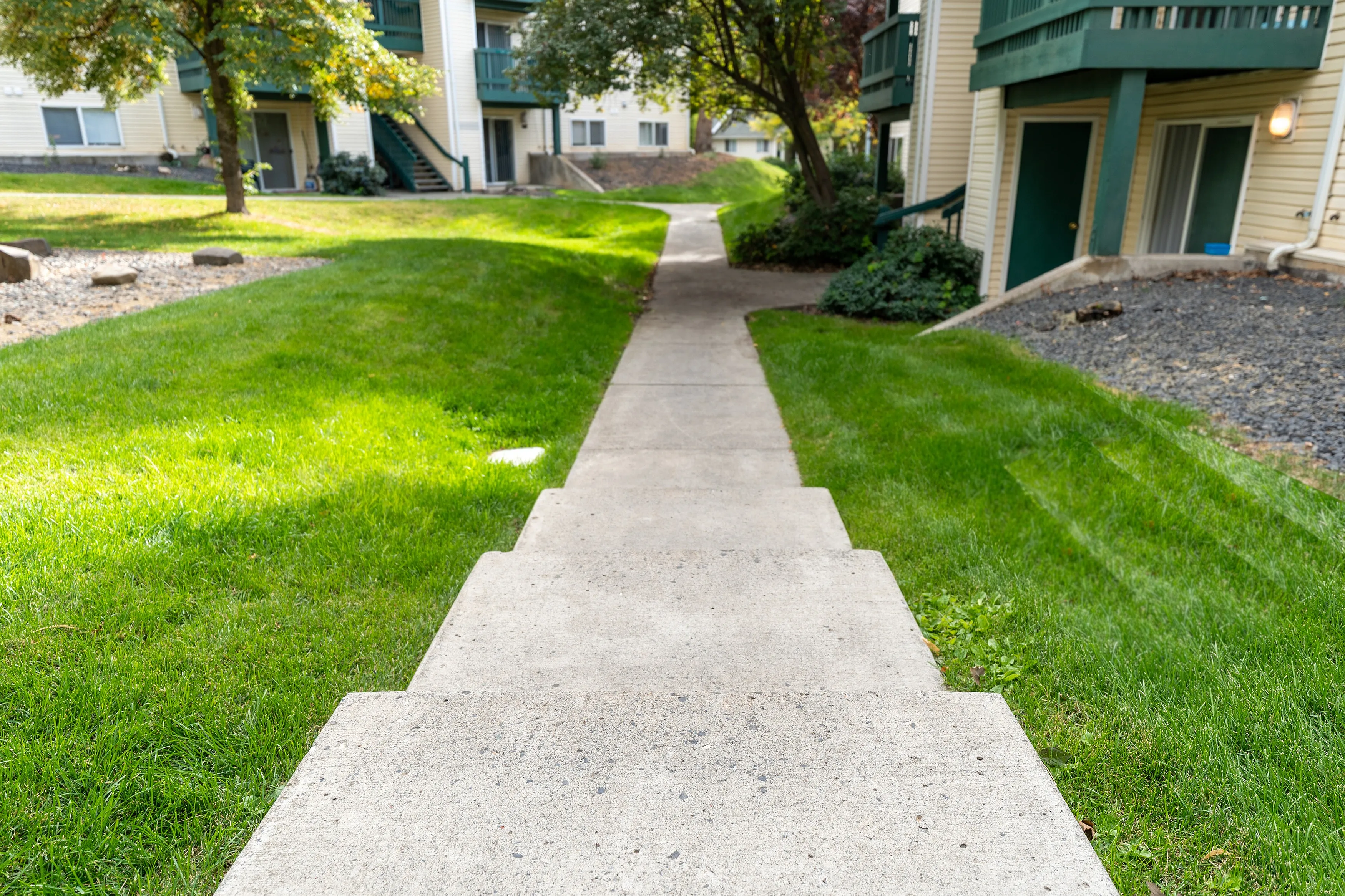 Inviting walkway leading to charming apartment entrance surrounded by lush greenery and mature trees.