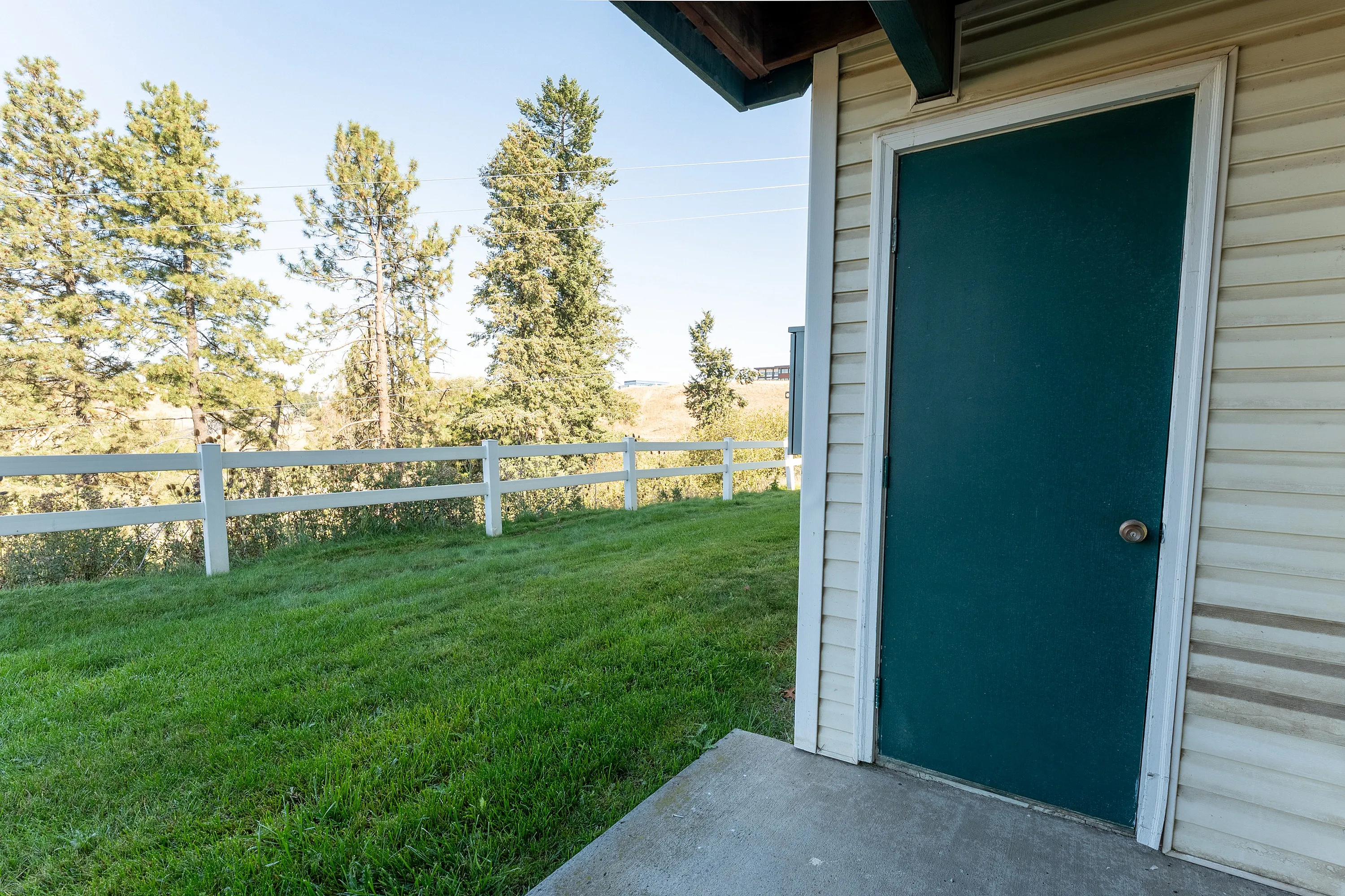 Charming outdoor view with lush green lawn and elegant white fencing next to a cozy home entrance.