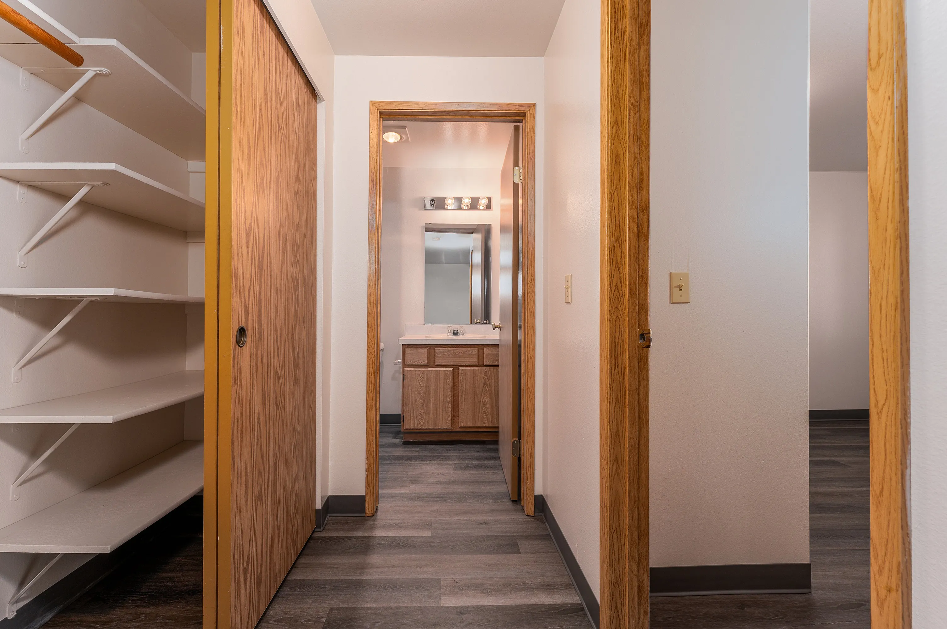 Inviting apartment hallway with contemporary wooden accents leading to a well-lit bathroom, featuring a sleek built-in closet with ample shelving.