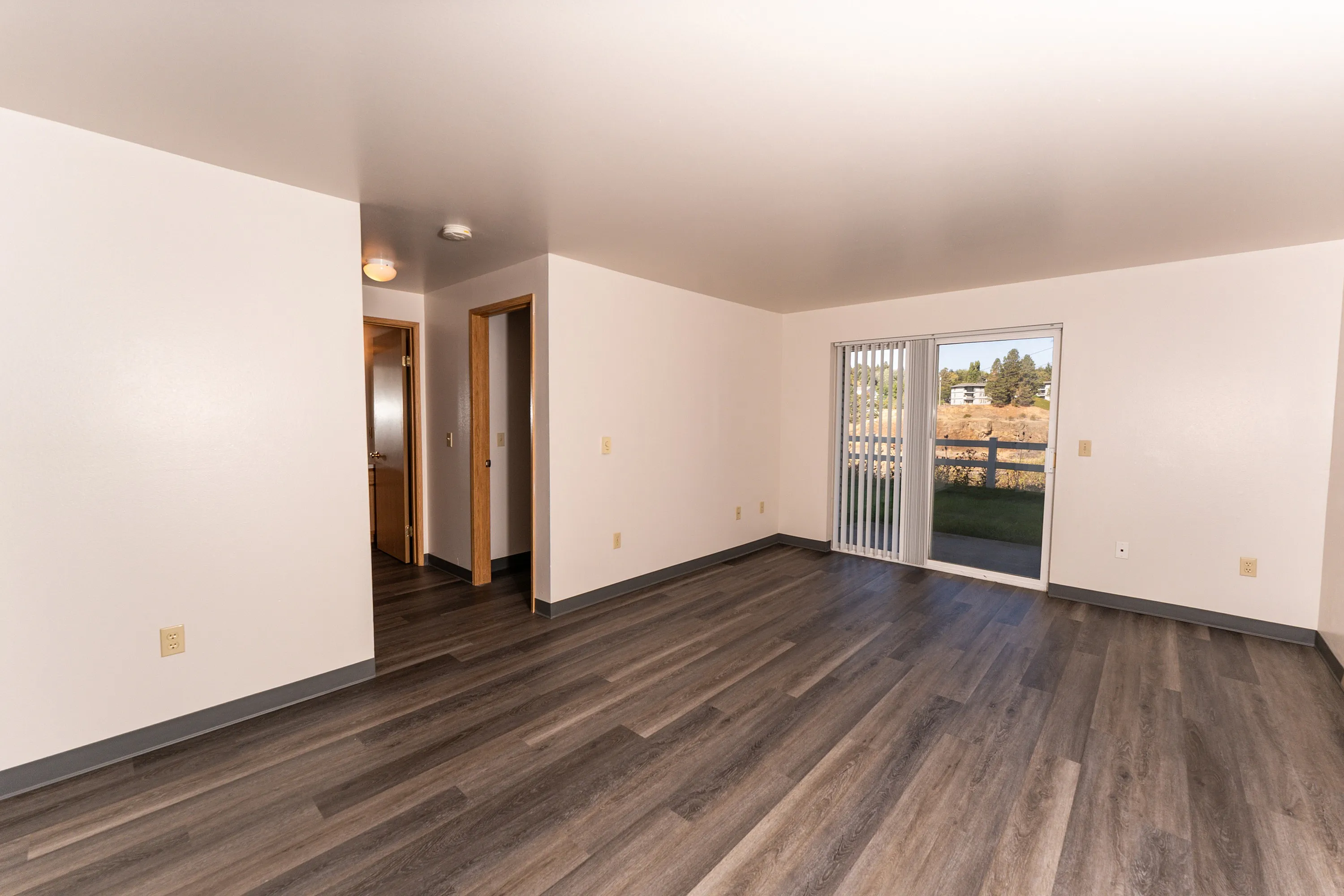 Bright and spacious living room with elegant wood flooring and large sliding doors opening to a scenic outdoor view.
