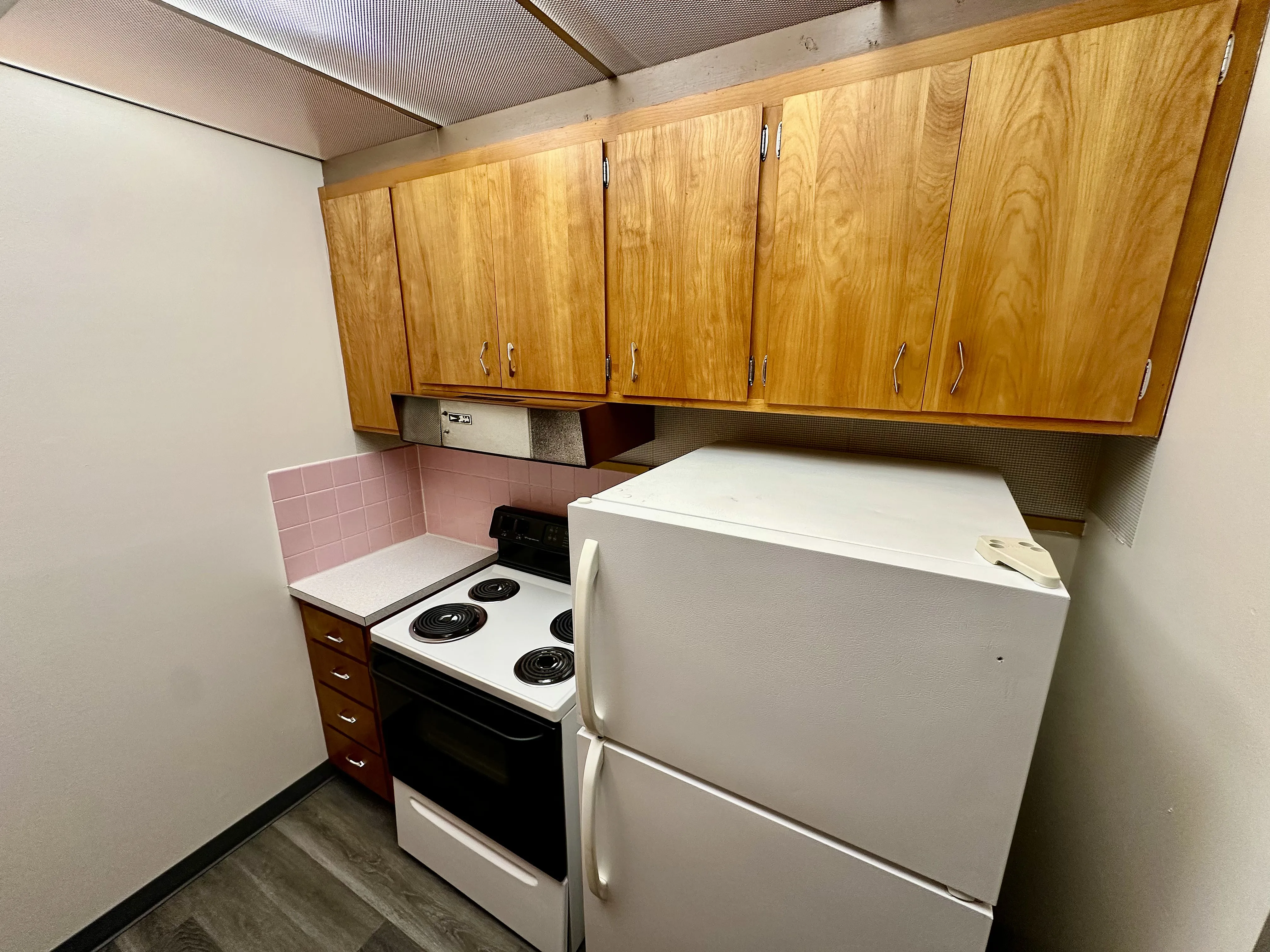 Cozy kitchen with warm wooden cabinets, sleek white appliances, and charming pink tile backsplash in a compact yet functional design.