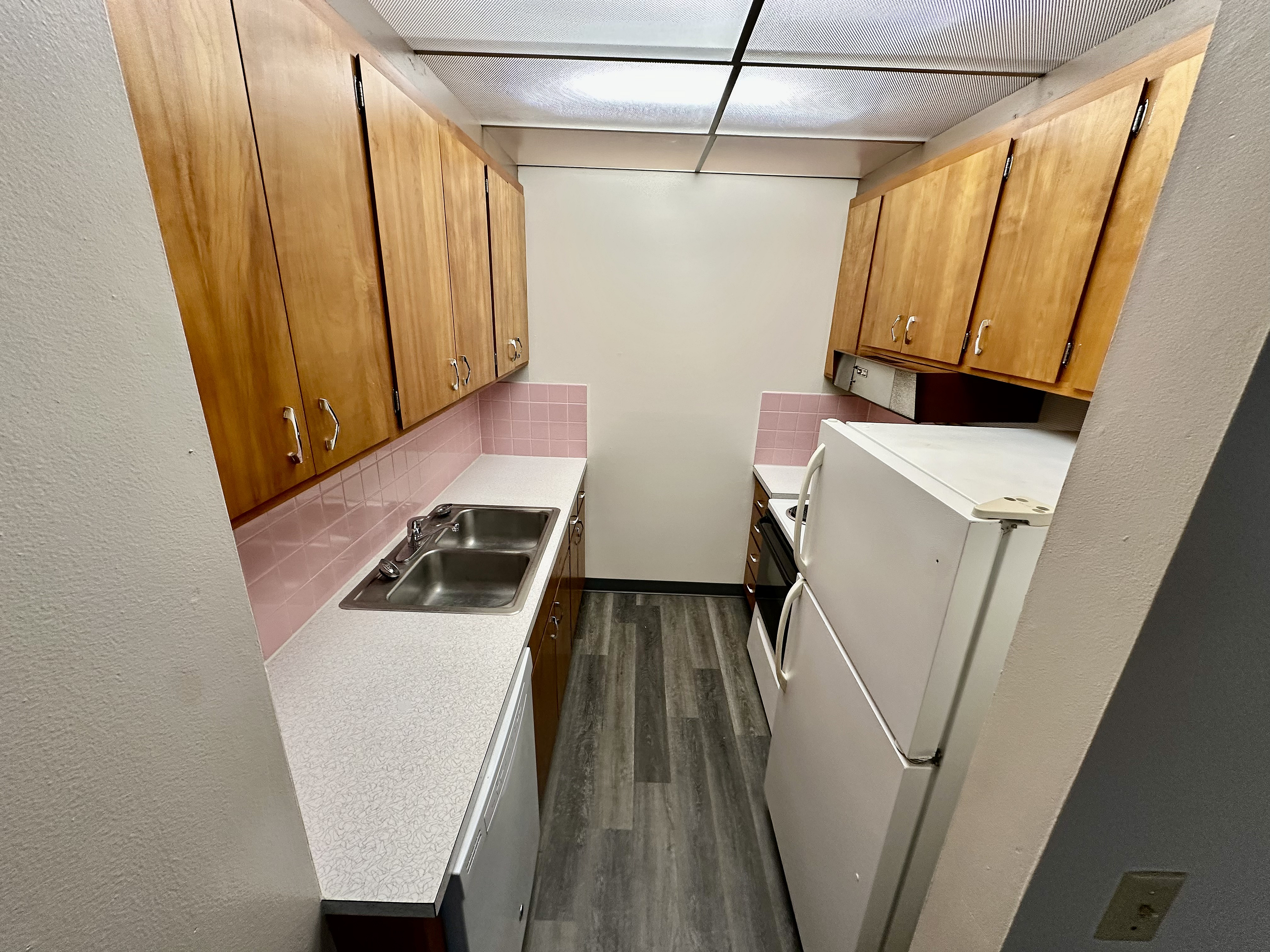 Charming kitchen with warm wooden cabinets, sleek countertops, and retro pink tile backsplash, perfect for cozy culinary adventures.