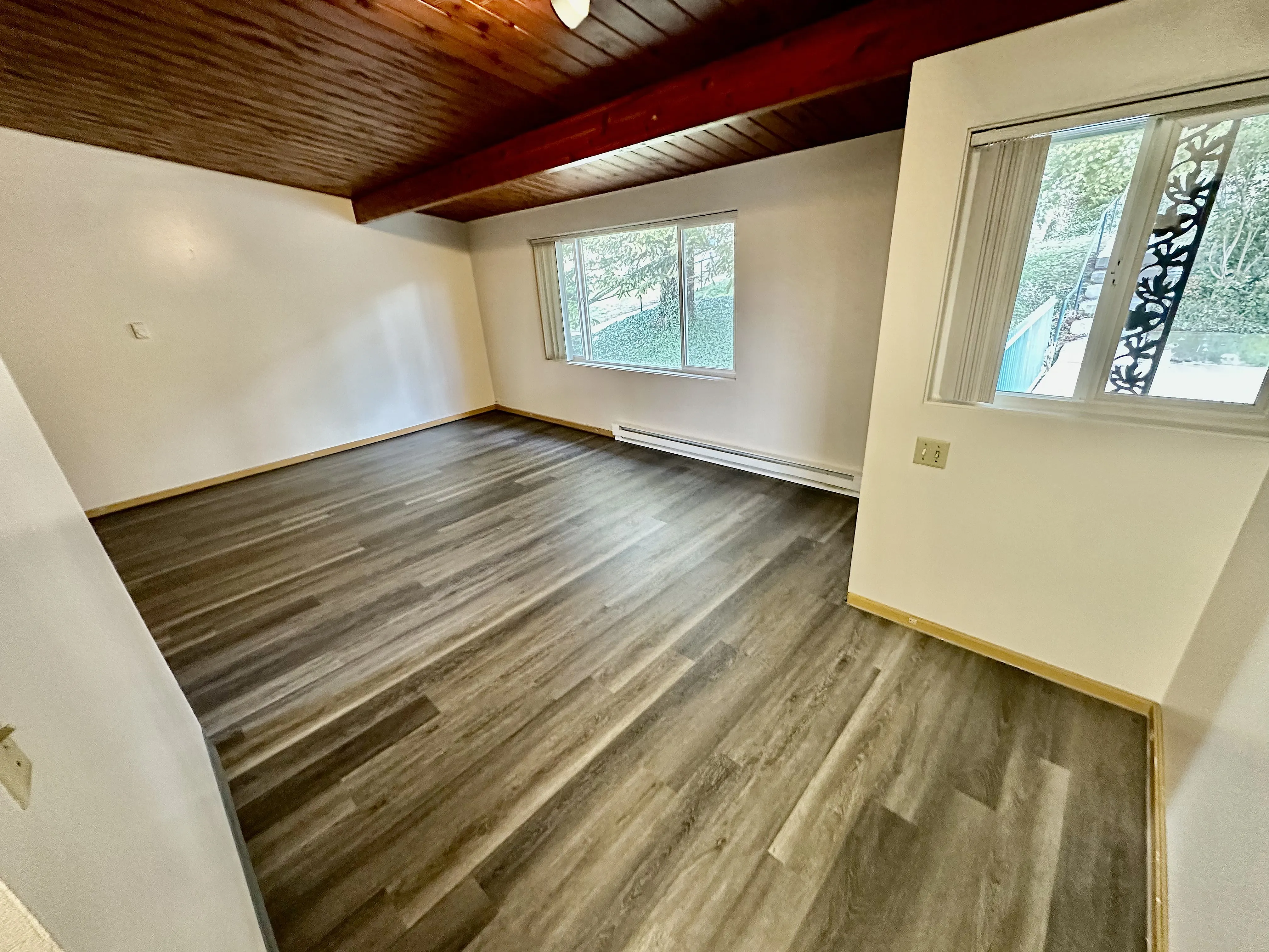 Bright and spacious room with elegant wood panel ceiling and modern vinyl flooring, large windows offering abundant natural light.
