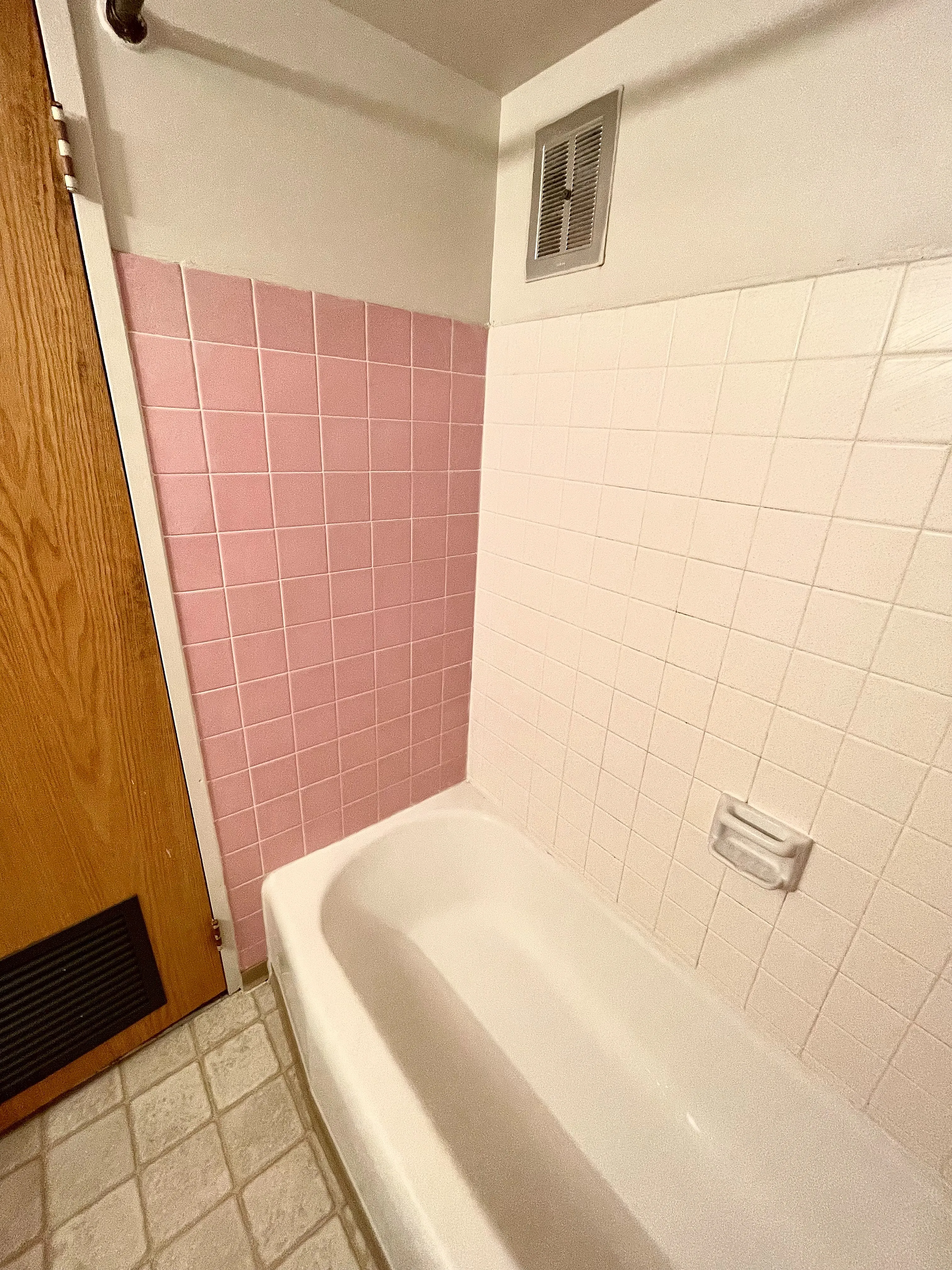 Charming bathroom with retro pink and white tiles featuring a cozy bathtub and elegant wooden door.